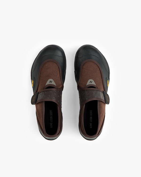 Top-down view of brown and black ALD / New Balance MT2 slip-on shoes with hook-and-loop closures and yellow Vibram tags.