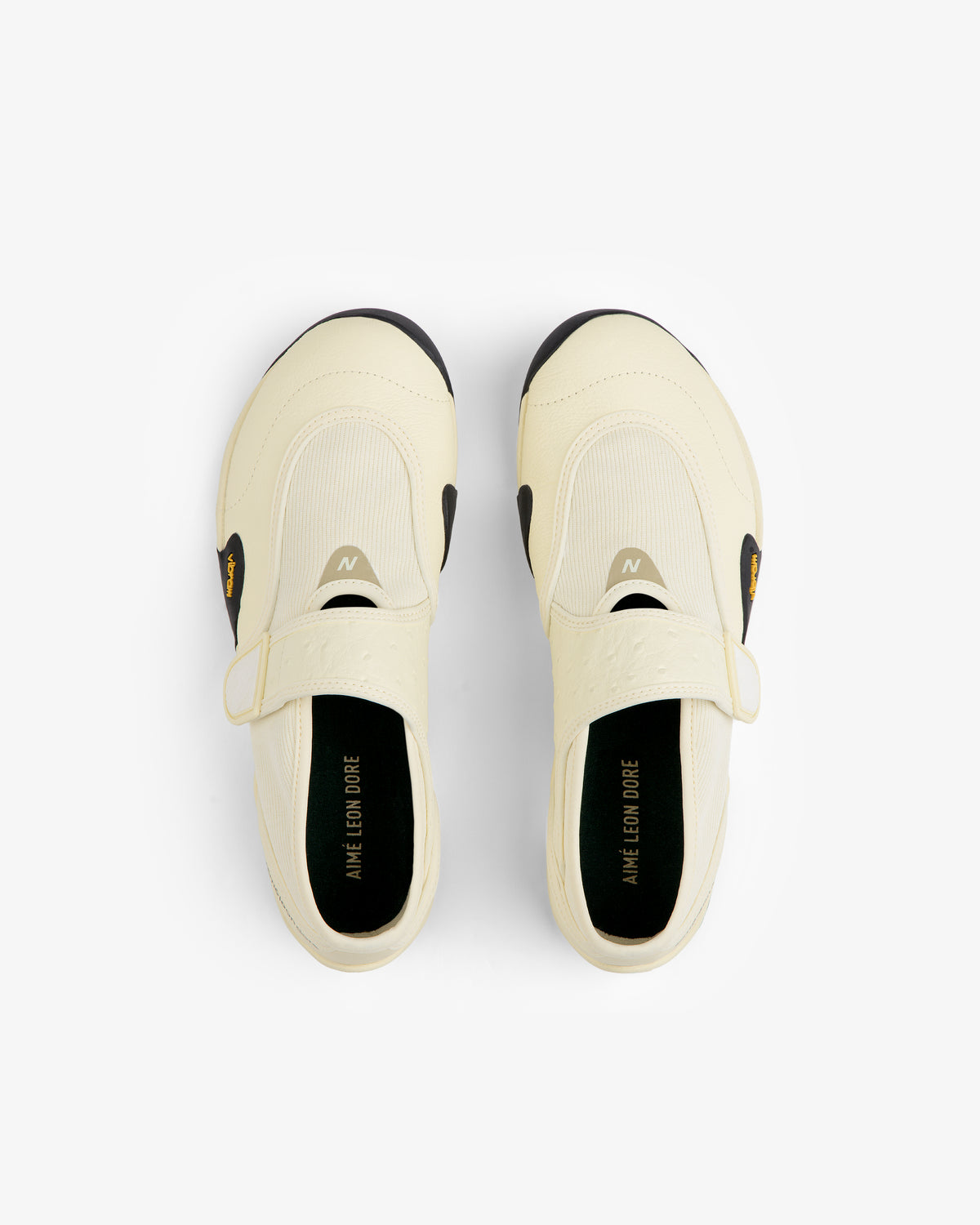 Top-down view of cream-colored ALD / New Balance MT2 slip-on shoes with straps, black Vibram soles, and black insoles.