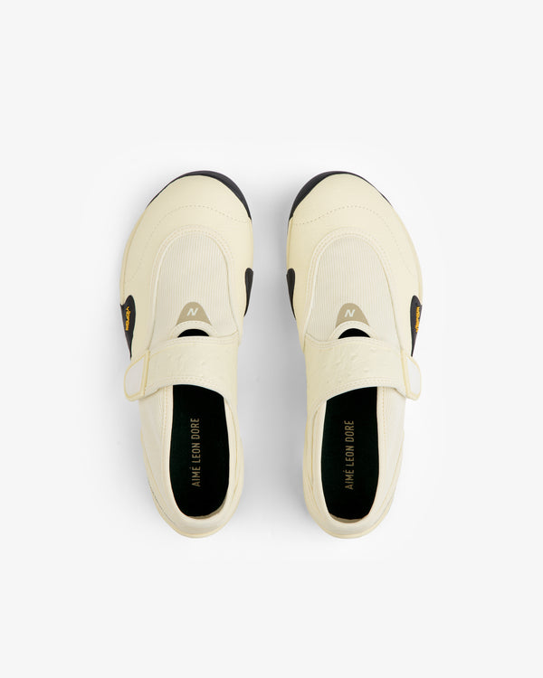Top-down view of cream-colored ALD / New Balance MT2 slip-on shoes with straps, black Vibram soles, and black insoles.