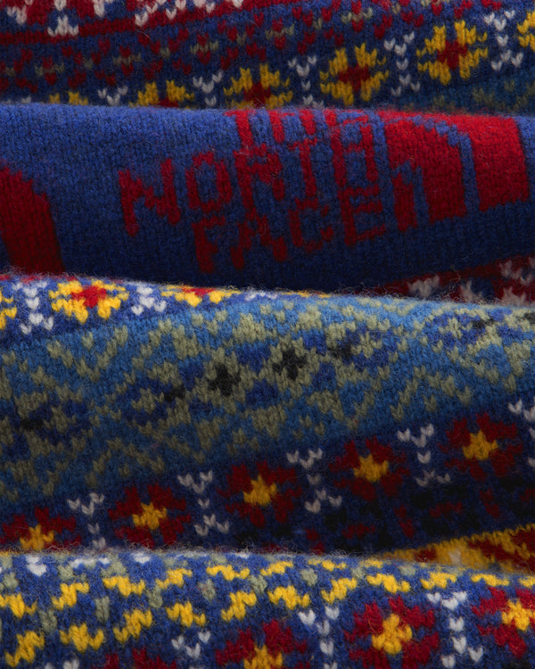 Close-up of the ALD/The North Face Fair Isle Knit Polo with red North Face text on a blue, patterned wool fabric.