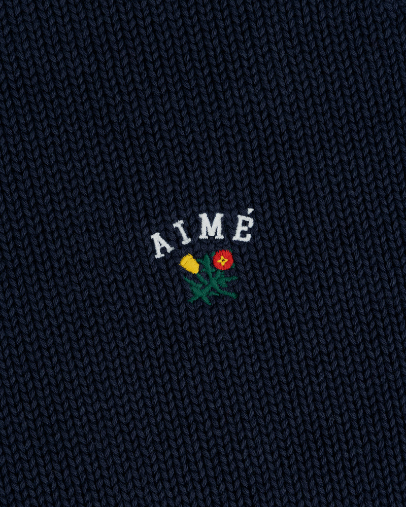 Dark blue Crest Raglan Sweater with AIMÉ embroidered above a small yellow and red flower design.