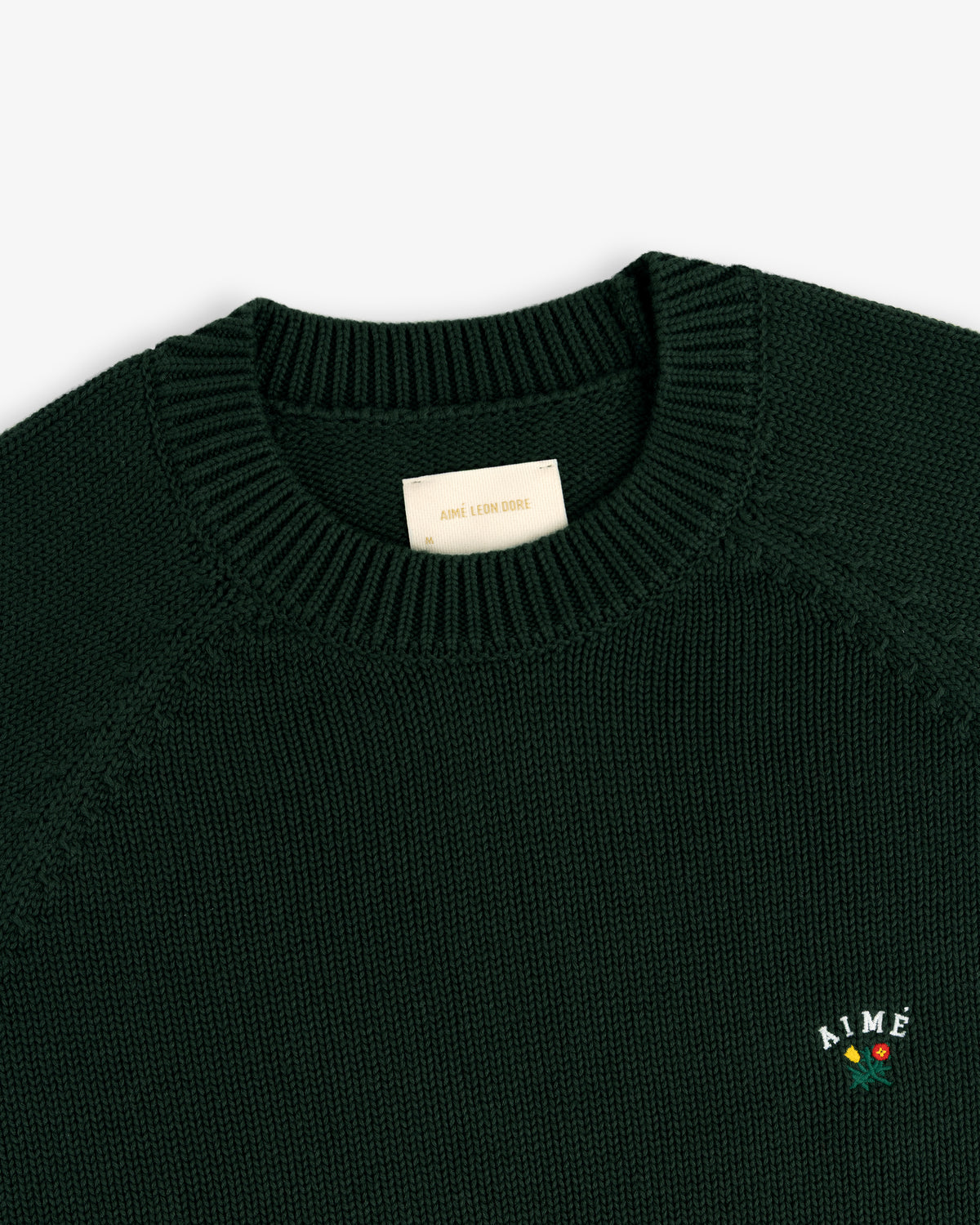 Crest Raglan Sweater: Dark green knit, ribbed collar, with AIMÉ text and rose embroidery near the hem.