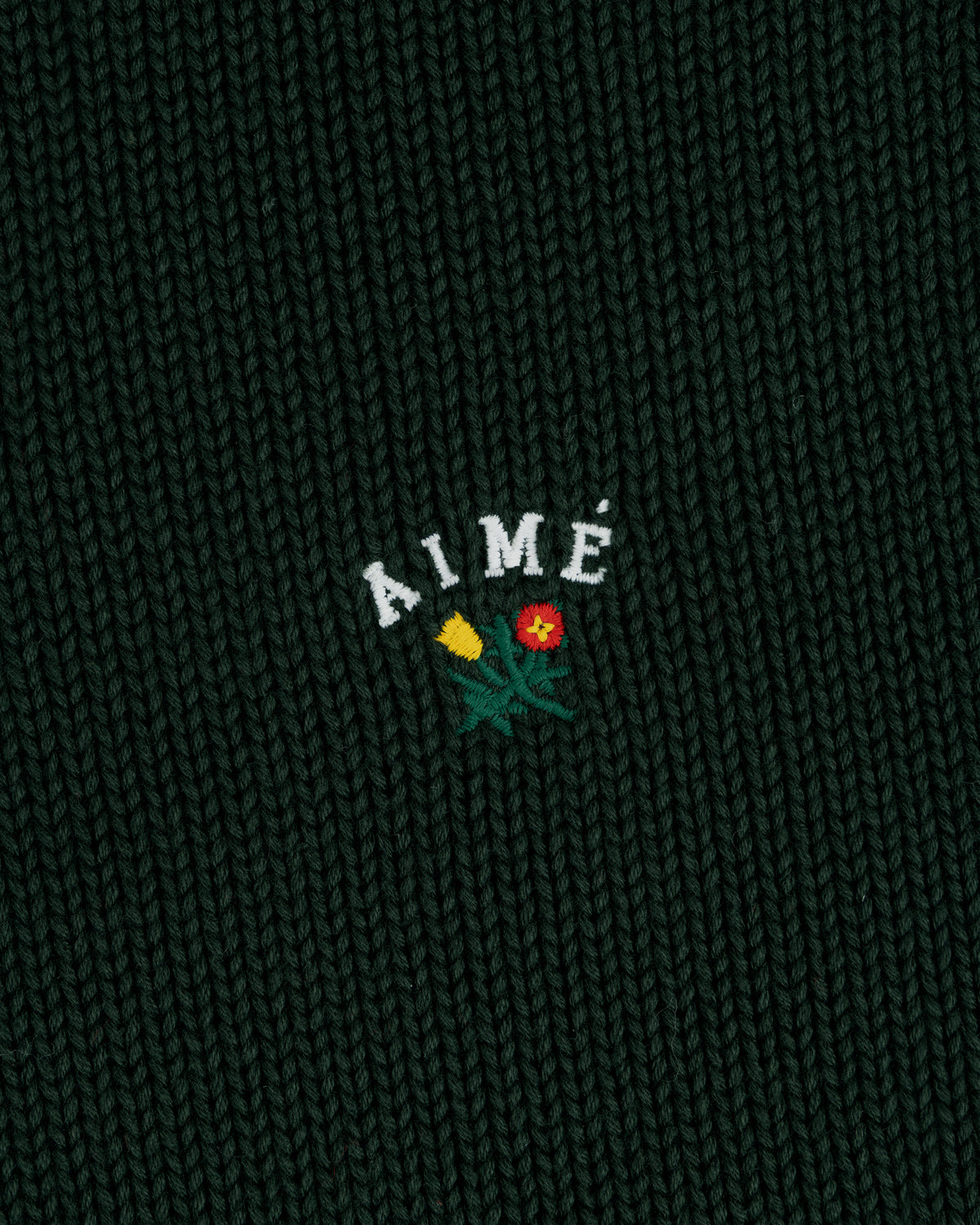 Dark green Crest Raglan Sweater with AIMÉ and two small flowers, one yellow and one red, embroidered beneath.