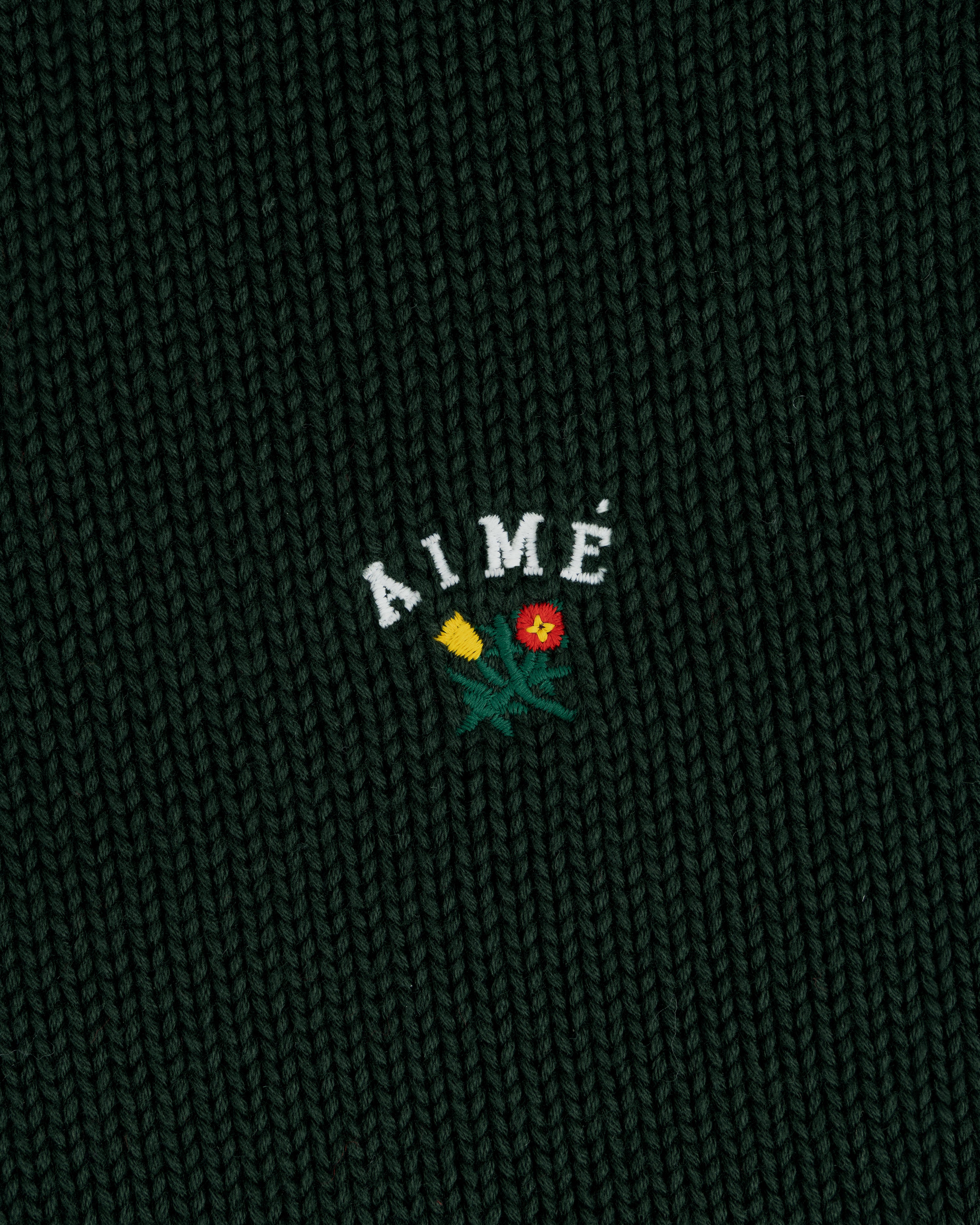 Dark green Crest Raglan Sweater with AIMÉ and two small flowers, one yellow and one red, embroidered beneath.
