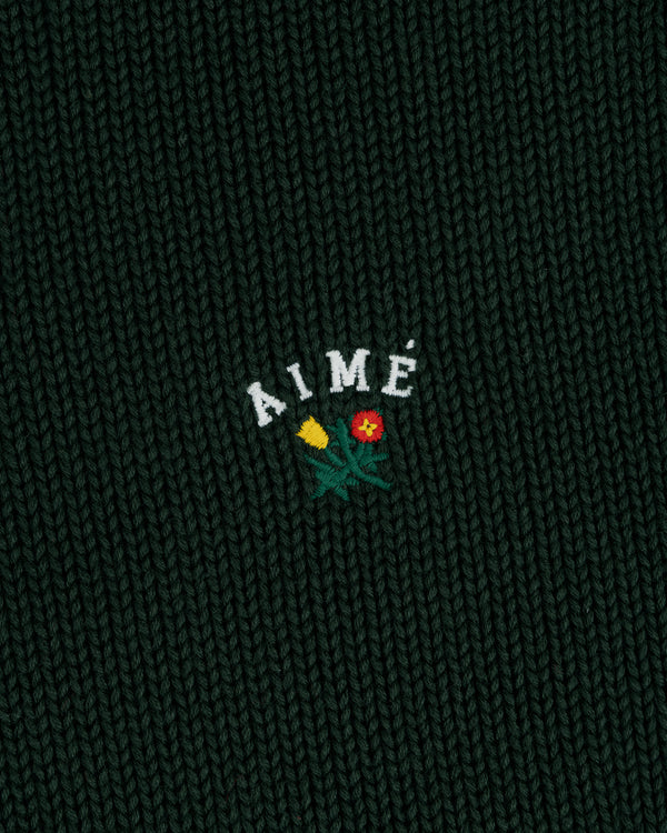 Dark green Crest Raglan Sweater with AIMÉ and two small flowers, one yellow and one red, embroidered beneath.