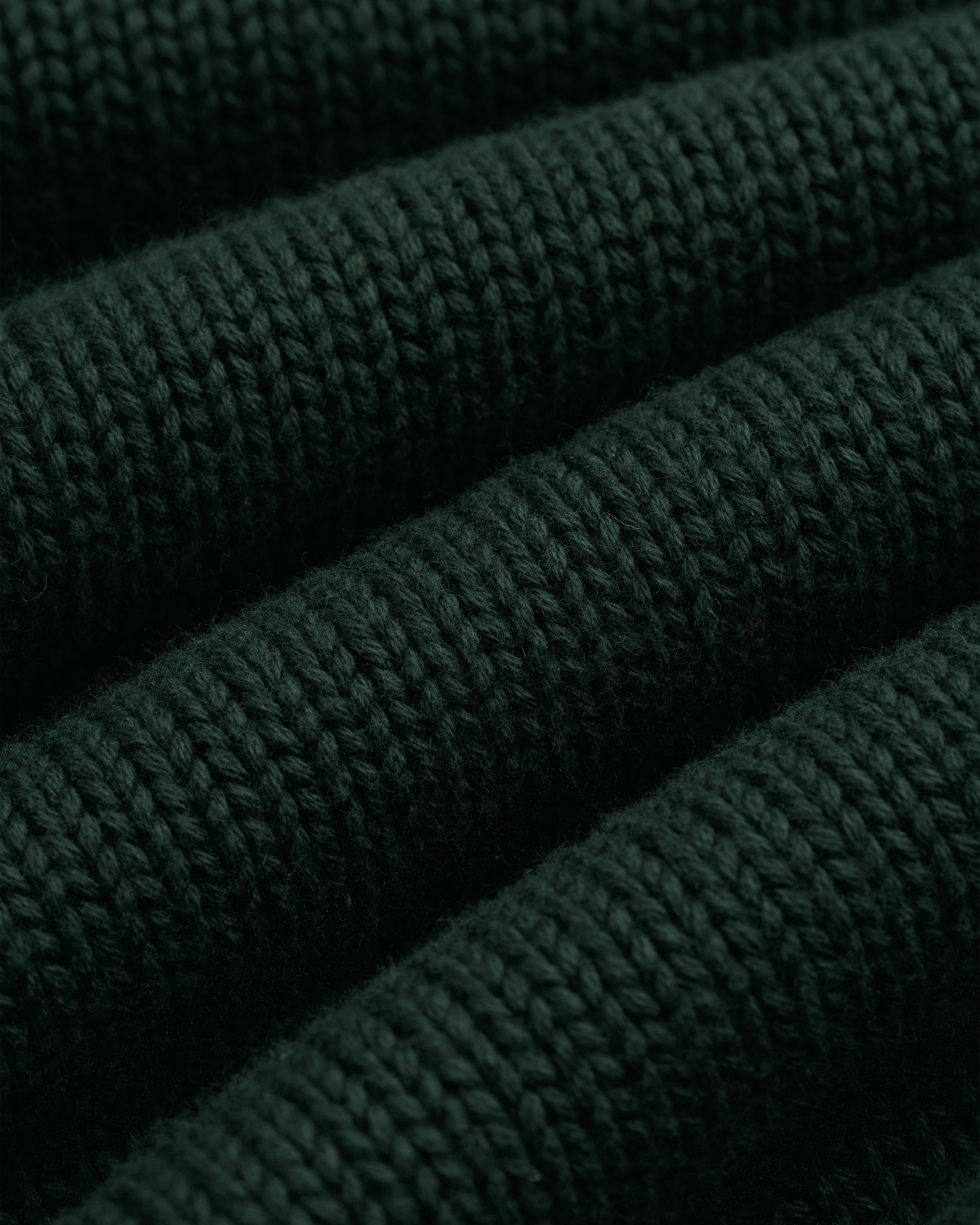 Close-up of Crest Raglan Sweater in dark green with horizontal ribbed texture and plush, thick yarn.