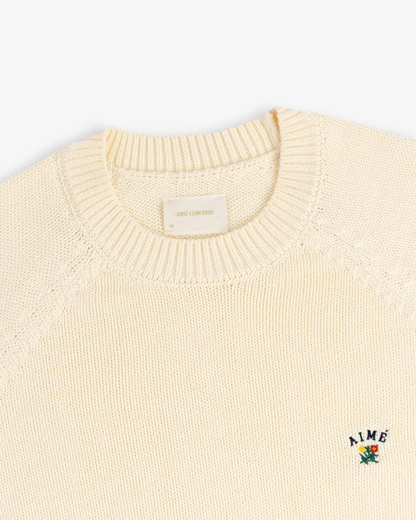 Crest Raglan Sweater: Cream knit with ribbed collar, small flower AIME logo embroidered on the chest.