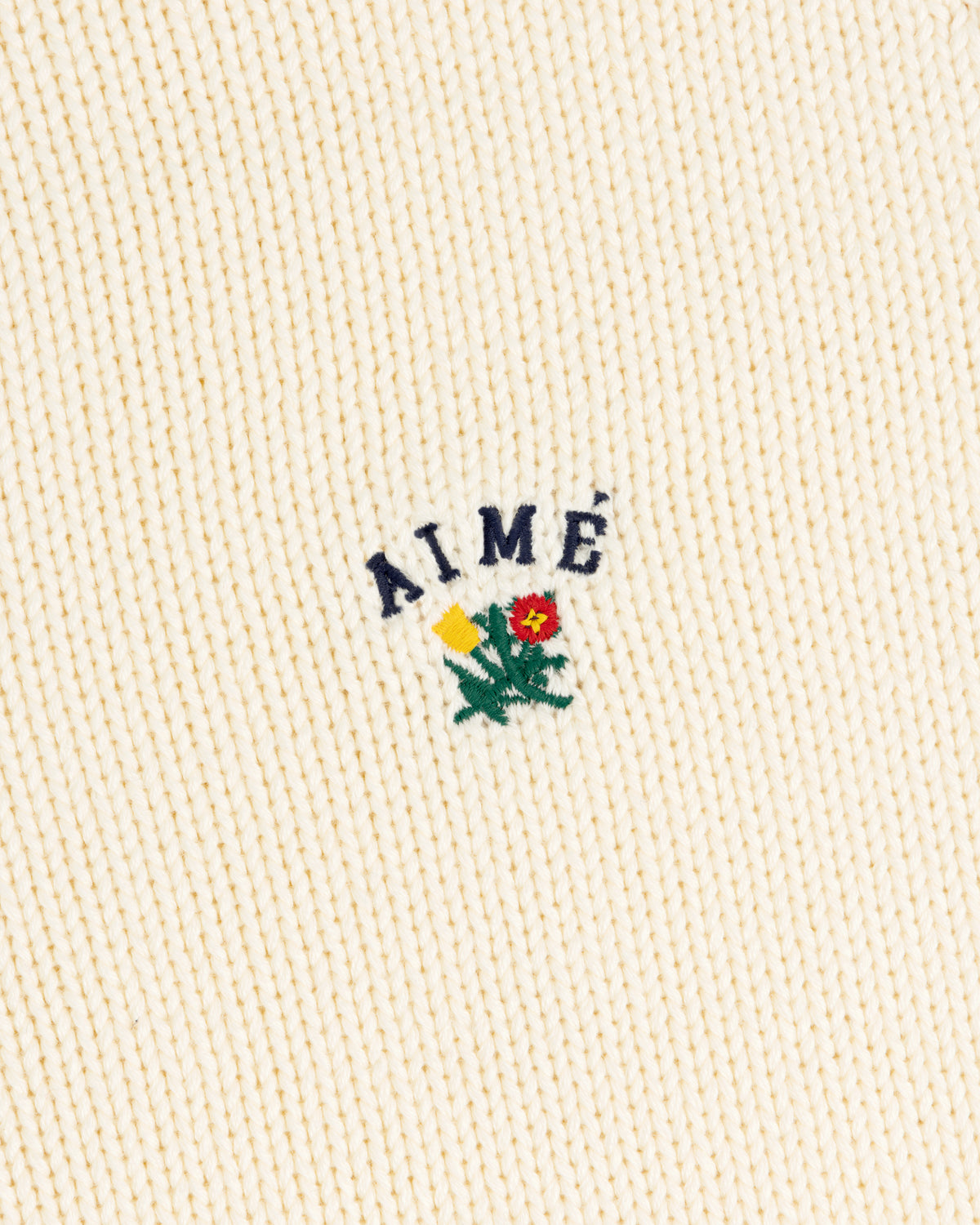 Cream Crest Raglan Sweater with AIMÉ text above yellow-red embroidered flowers and green leaves.