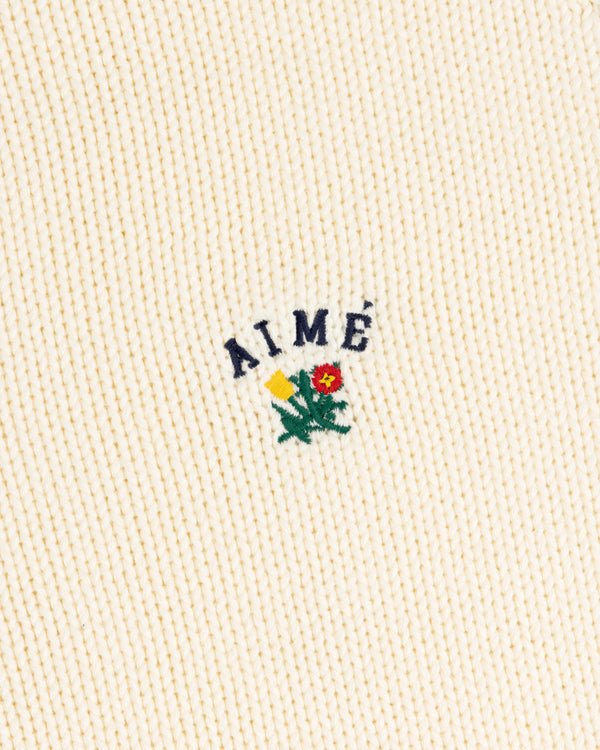 Cream Crest Raglan Sweater with AIMÉ text above yellow-red embroidered flowers and green leaves.