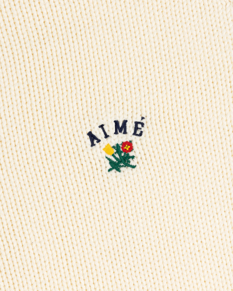 Cream Crest Raglan Sweater with AIMÉ text above yellow-red embroidered flowers and green leaves.