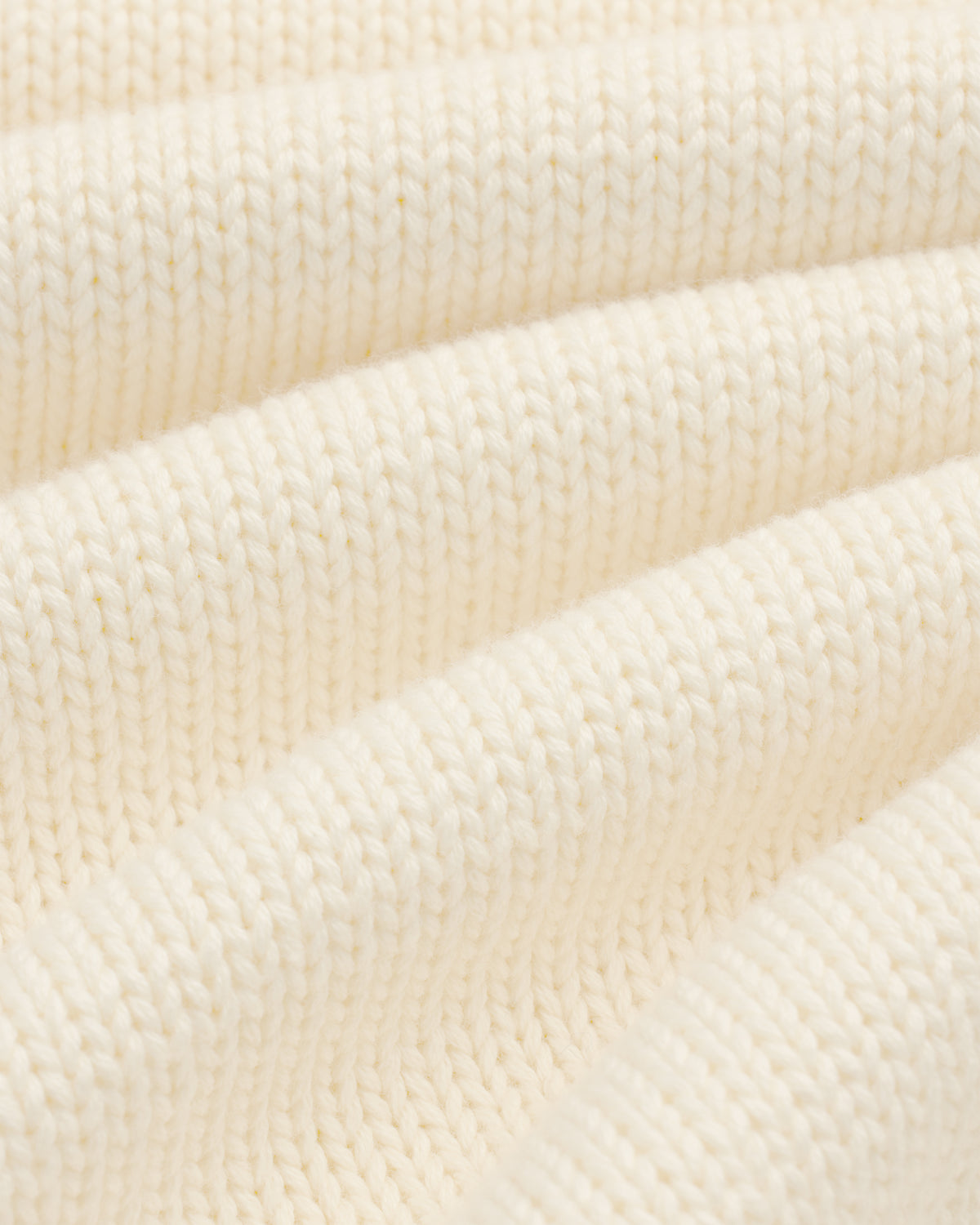 Close-up of Crest Raglan Sweater in cream ribbed knit, highlighting texture and soft, curved folds.