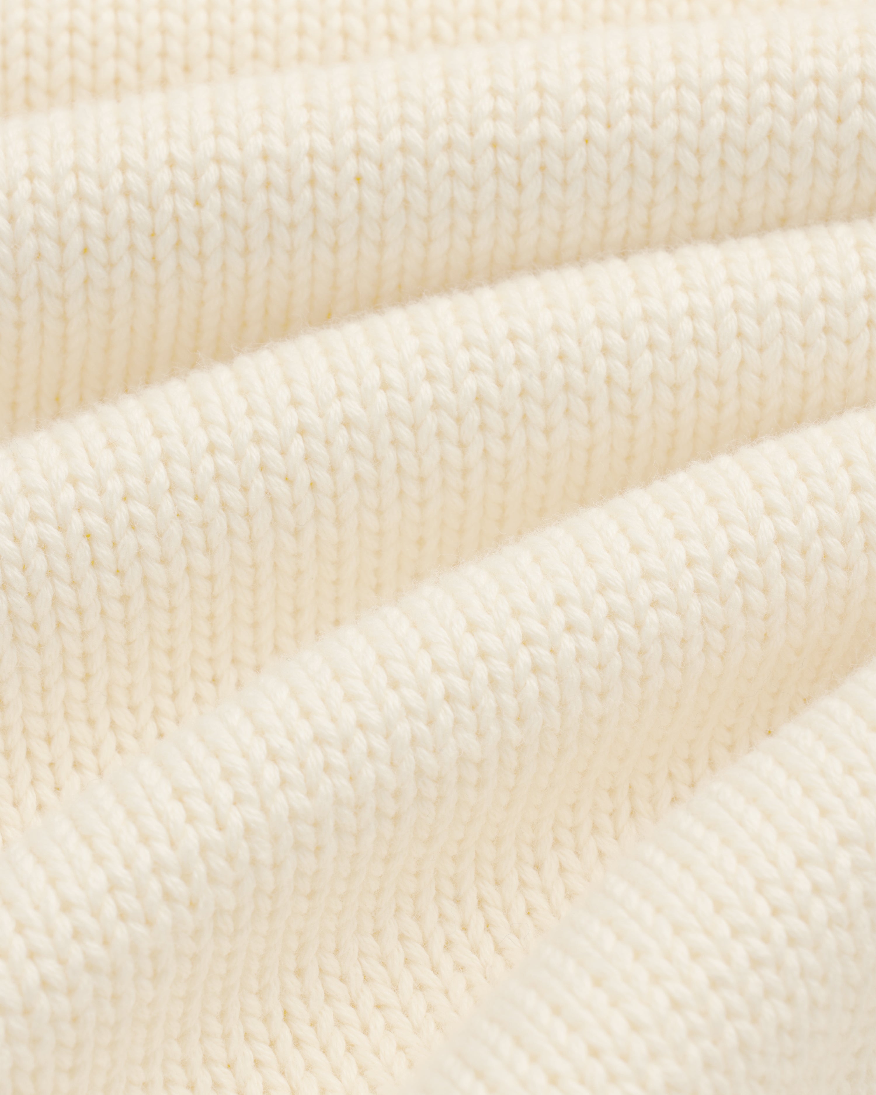 Close-up of Crest Raglan Sweater in cream ribbed knit, highlighting texture and soft, curved folds.