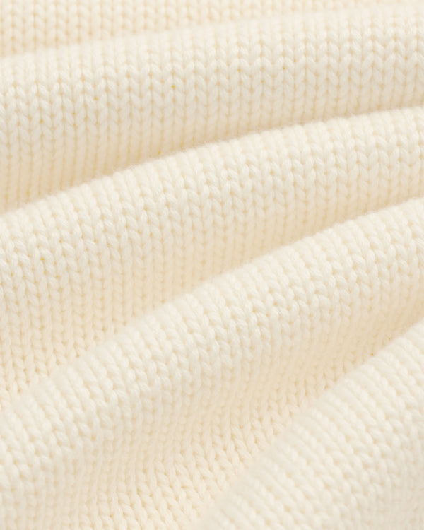 Close-up of Crest Raglan Sweater in cream ribbed knit, highlighting texture and soft, curved folds.