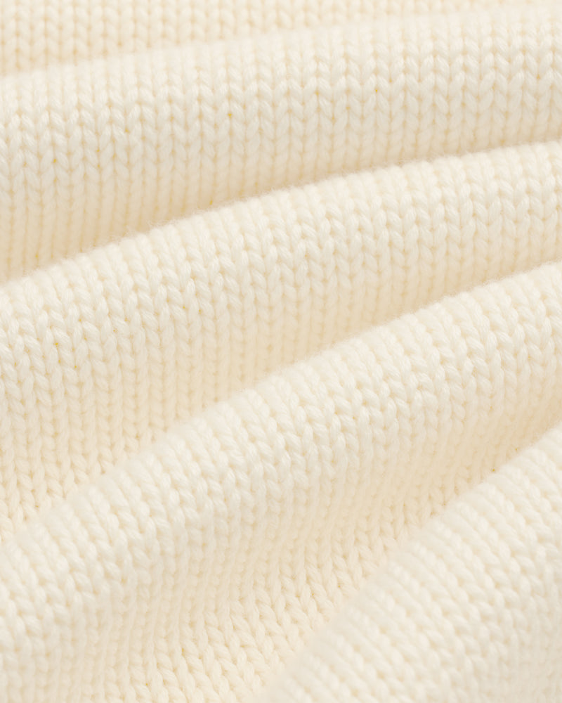 Close-up of Crest Raglan Sweater in cream ribbed knit, highlighting texture and soft, curved folds.