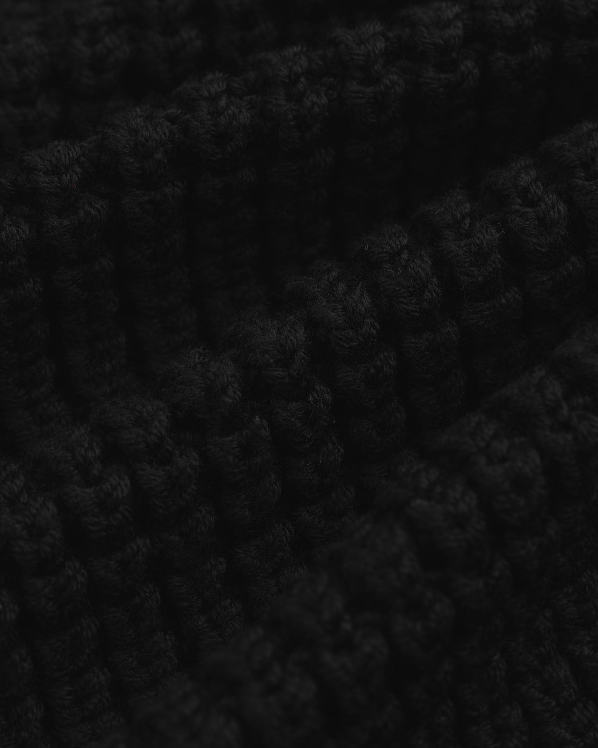 Close-up of the thick, black ribbed knit fabric of a Merino Wool Full Zip Sweater.