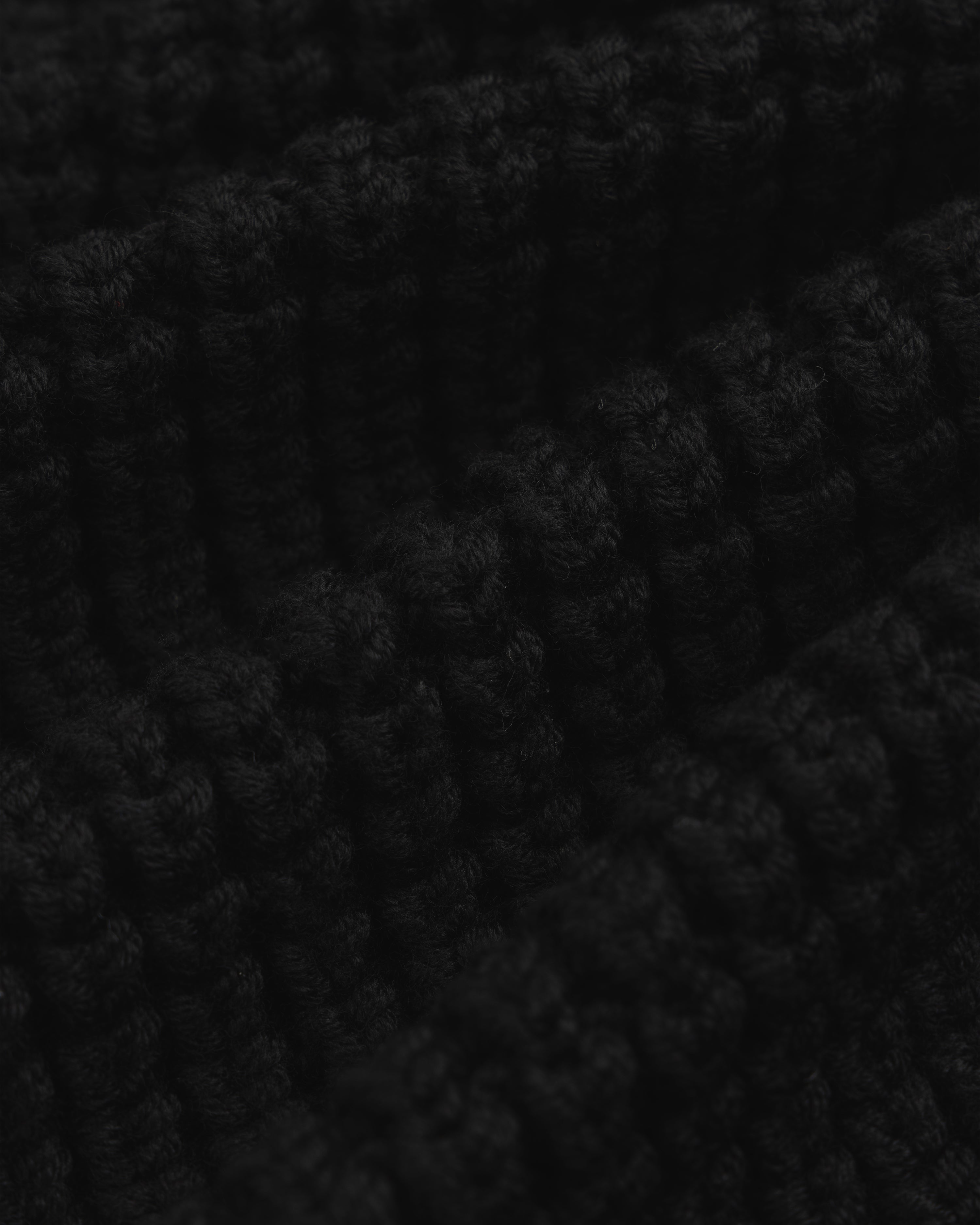 Close-up of the thick, black ribbed knit fabric of a Merino Wool Full Zip Sweater.