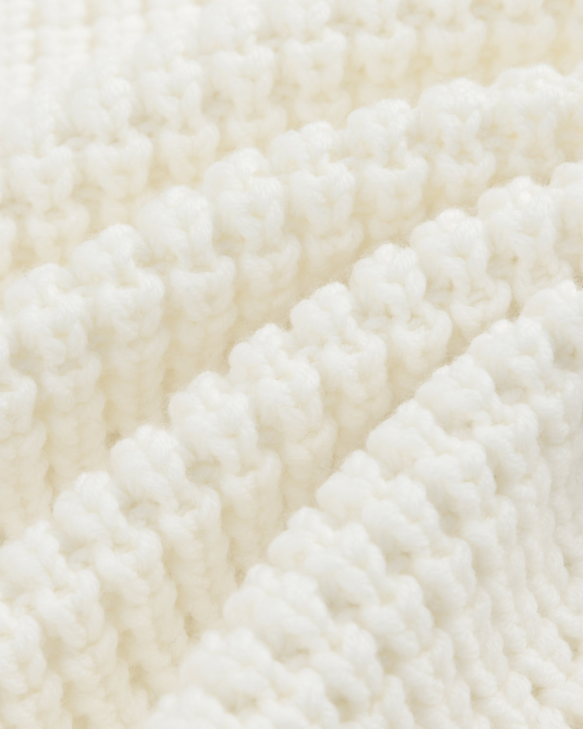 Close-up of white ribbed knit fabric on a Merino Wool Full Zip Sweater, shown with diagonal folds.