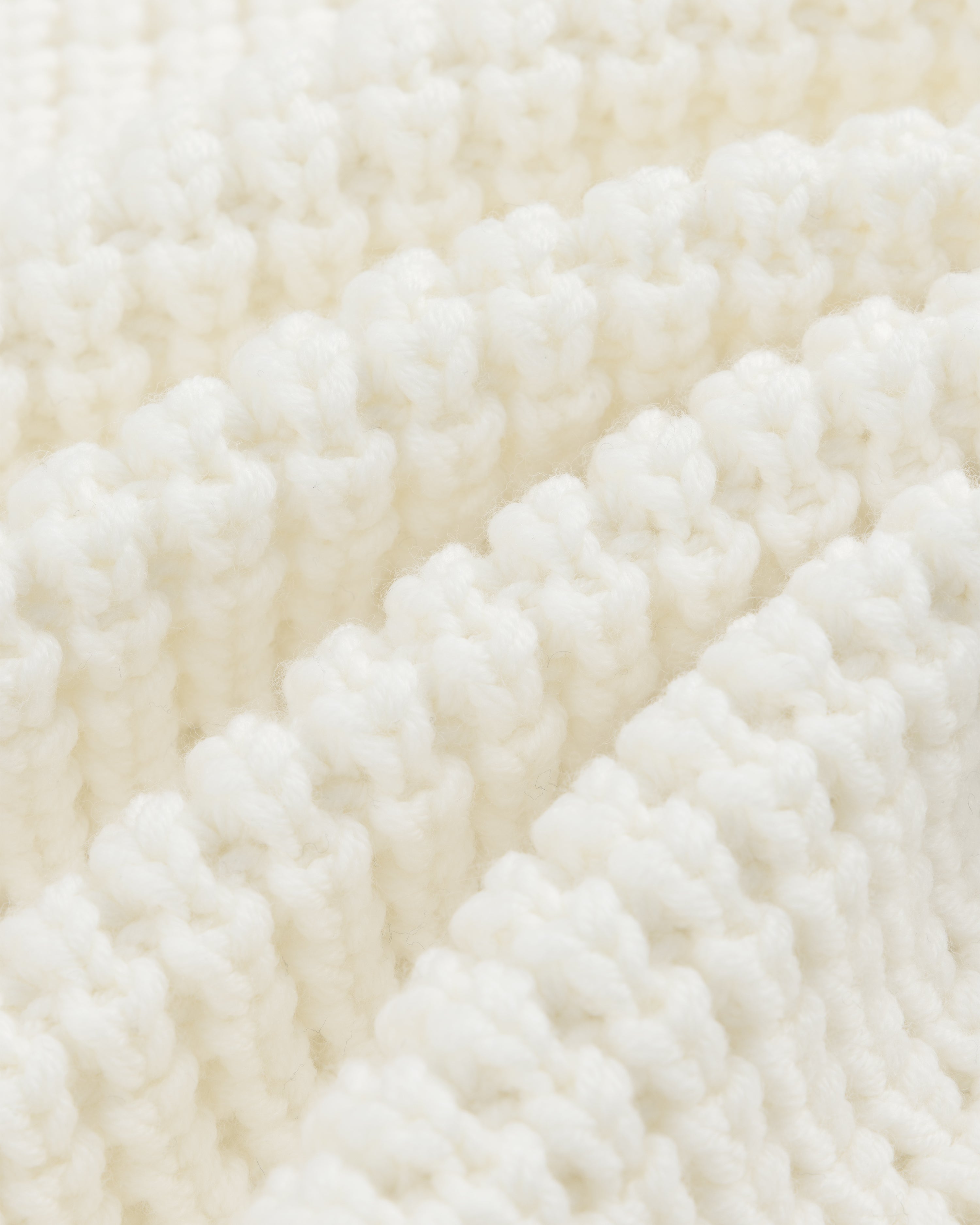 Close-up of white ribbed knit fabric on a Merino Wool Full Zip Sweater, shown with diagonal folds.