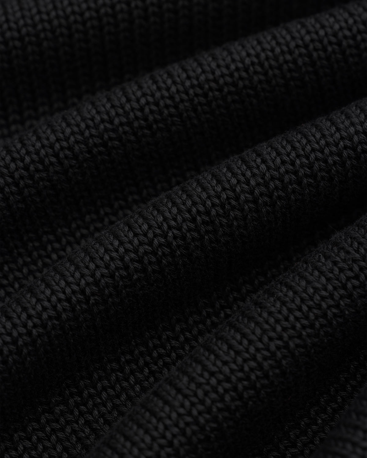 Close-up of black Knit Pocket Crewneck Sweater fabric featuring deep, horizontal folds.