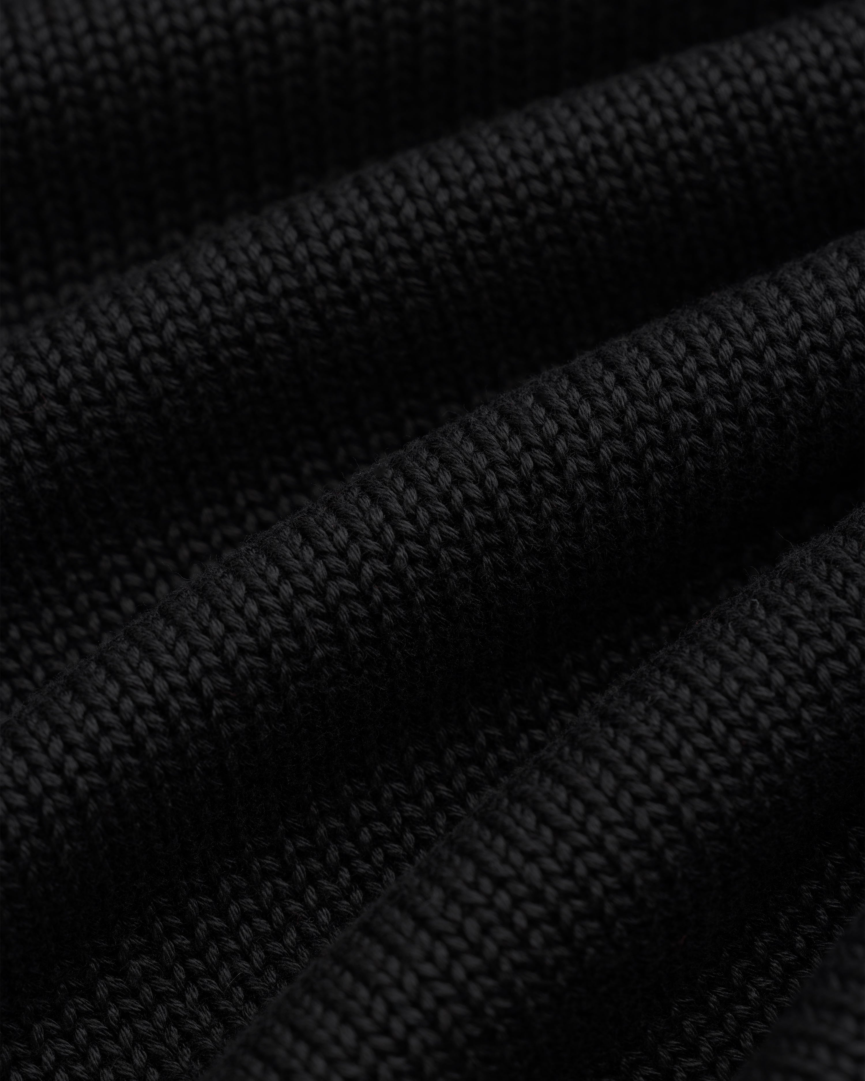 Close-up of black Knit Pocket Crewneck Sweater fabric featuring deep, horizontal folds.