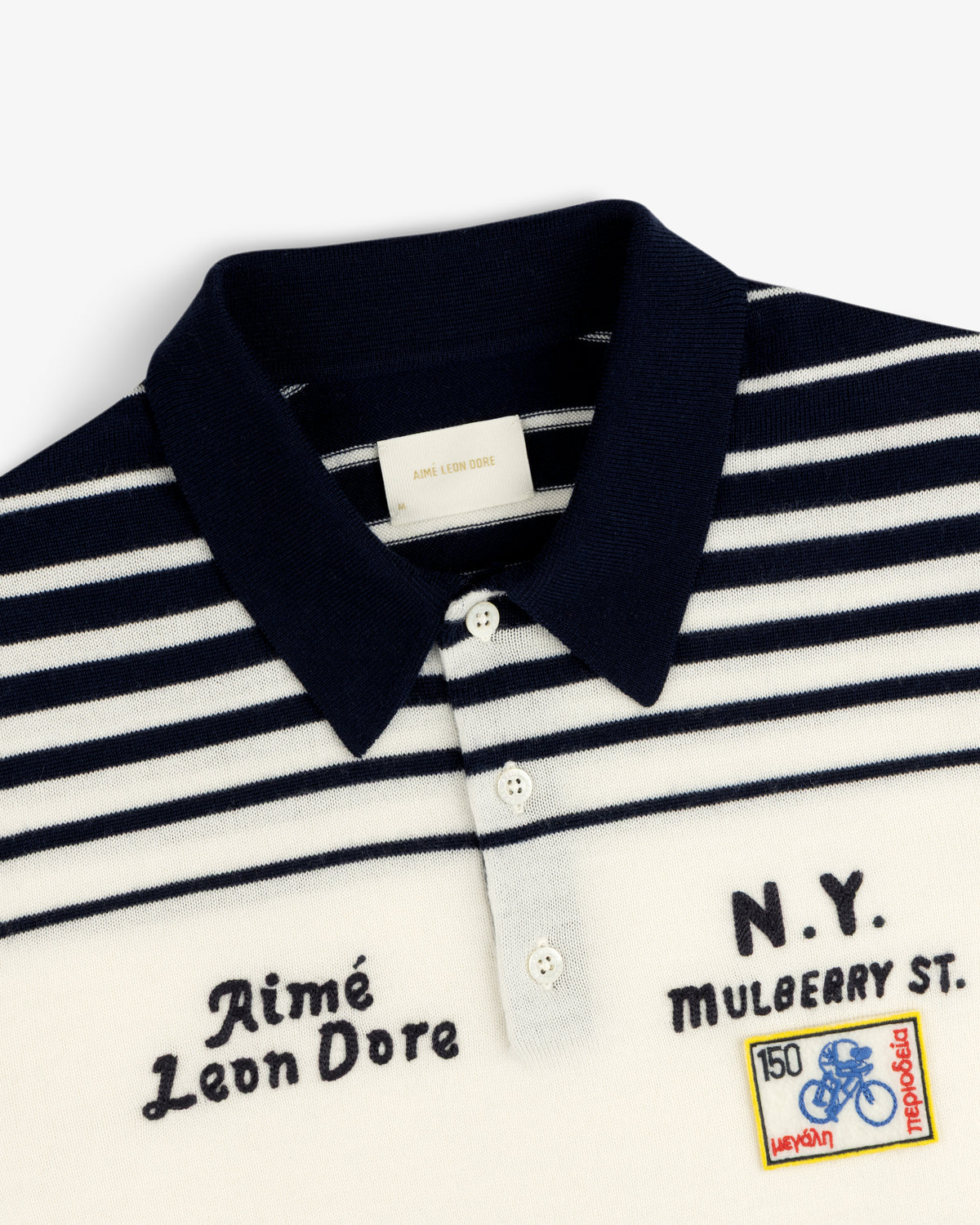 Closeup of a navy and white striped Merino Wool Knit Cycling Polo with embroidered patches and chest text.