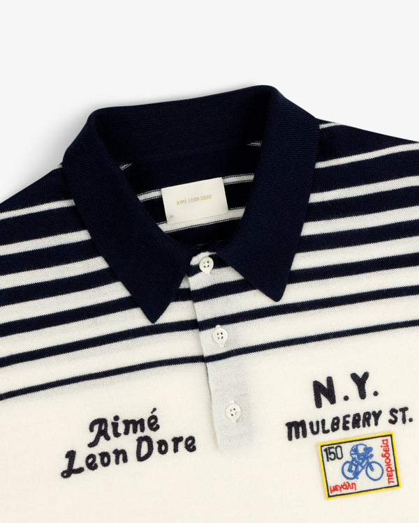 Closeup of a navy and white striped Merino Wool Knit Cycling Polo with embroidered patches and chest text.