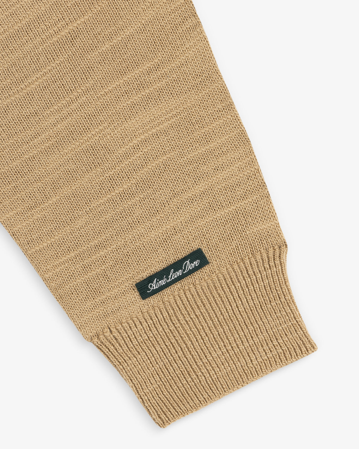 Tan Slub Merino Wool Sweater sleeve with a ribbed cuff and a small label featuring a brand name.