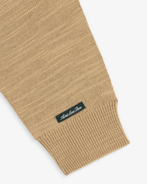 Tan Slub Merino Wool Sweater sleeve with a ribbed cuff and a small label featuring a brand name.