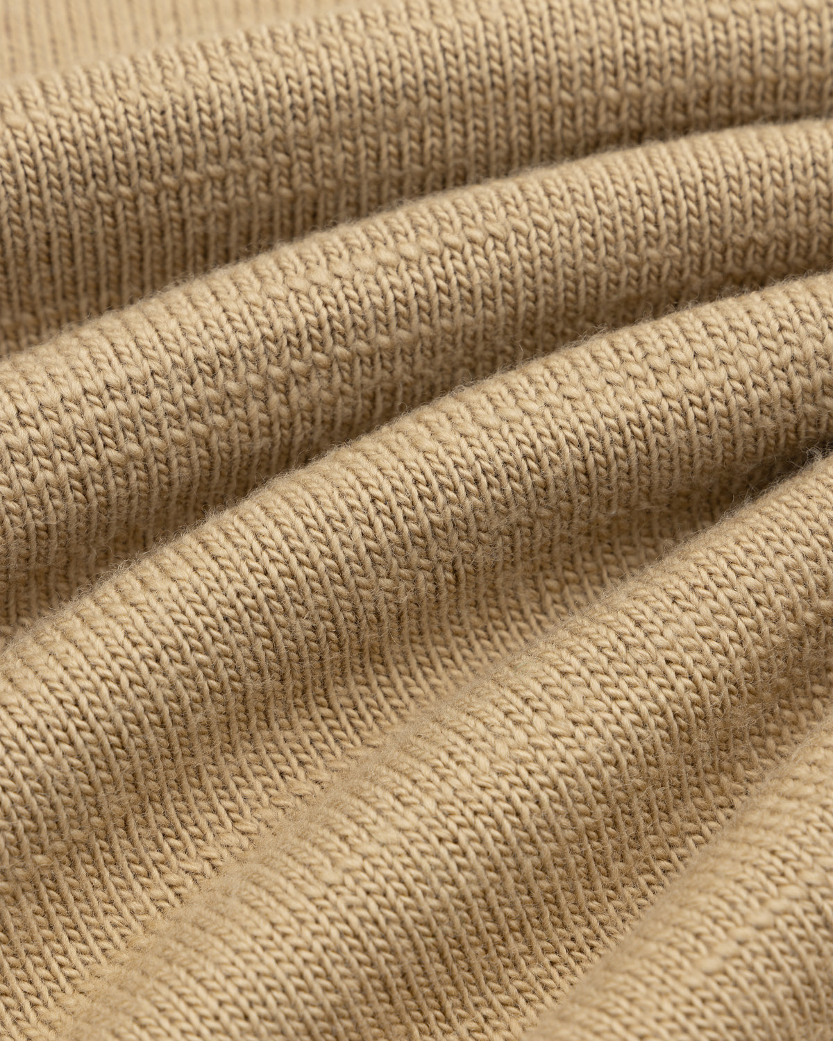 Close-up of the Slub Merino Wool Sweater in tan knit fabric with visible folds.
