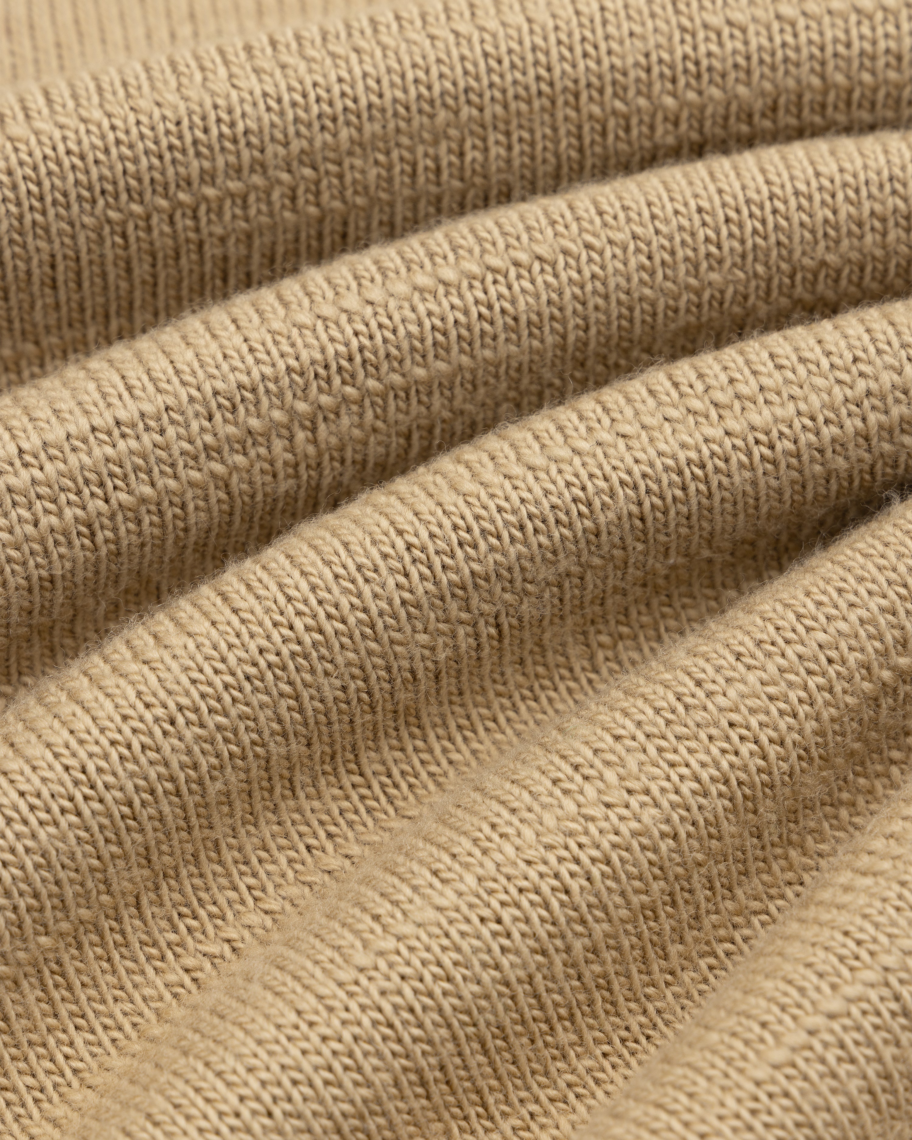 Close-up of the Slub Merino Wool Sweater in tan knit fabric with visible folds.