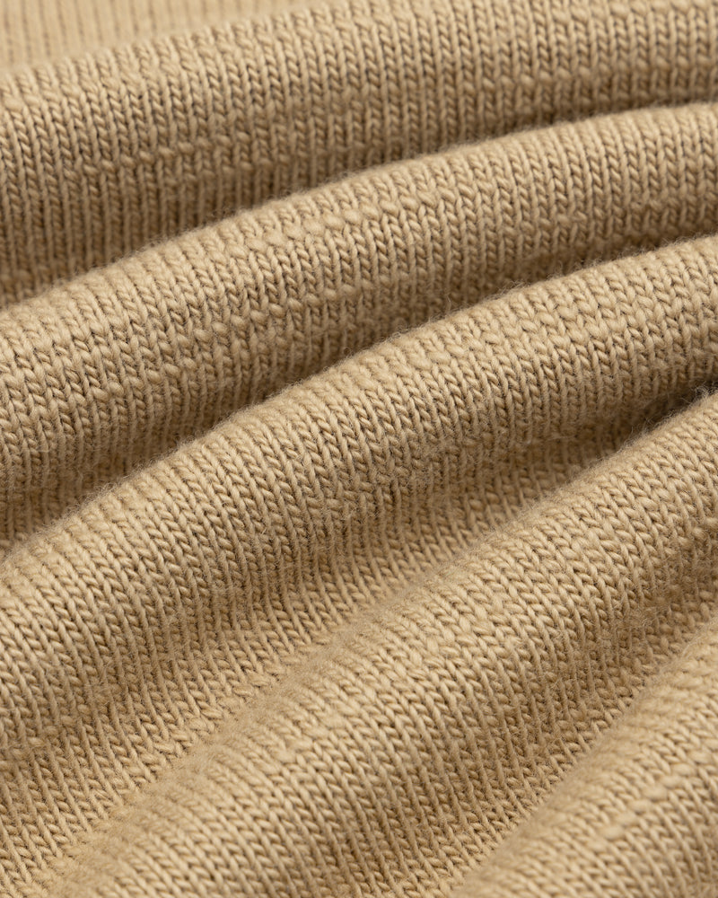 Close-up of the Slub Merino Wool Sweater in tan knit fabric with visible folds.