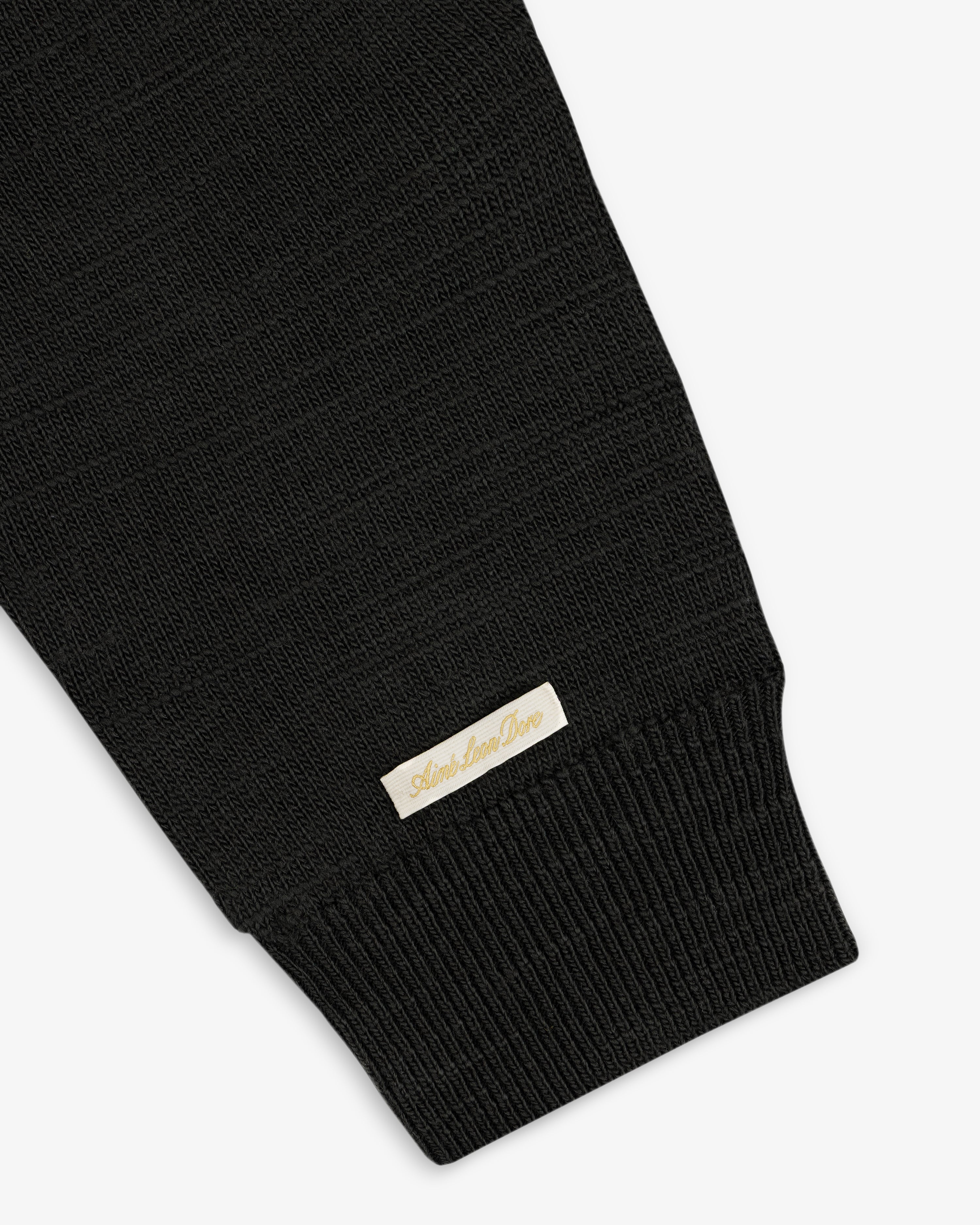 Black Slub Merino Wool Sweater sleeve featuring a ribbed cuff and a small rectangular label near the wrist.