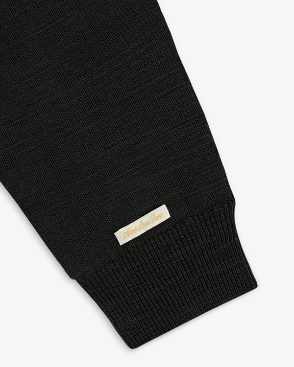Black Slub Merino Wool Sweater sleeve featuring a ribbed cuff and a small rectangular label near the wrist.