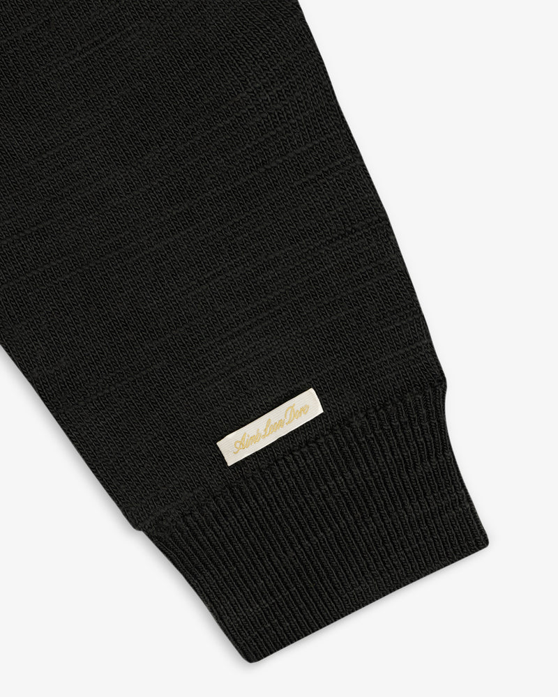 Black Slub Merino Wool Sweater sleeve featuring a ribbed cuff and a small rectangular label near the wrist.