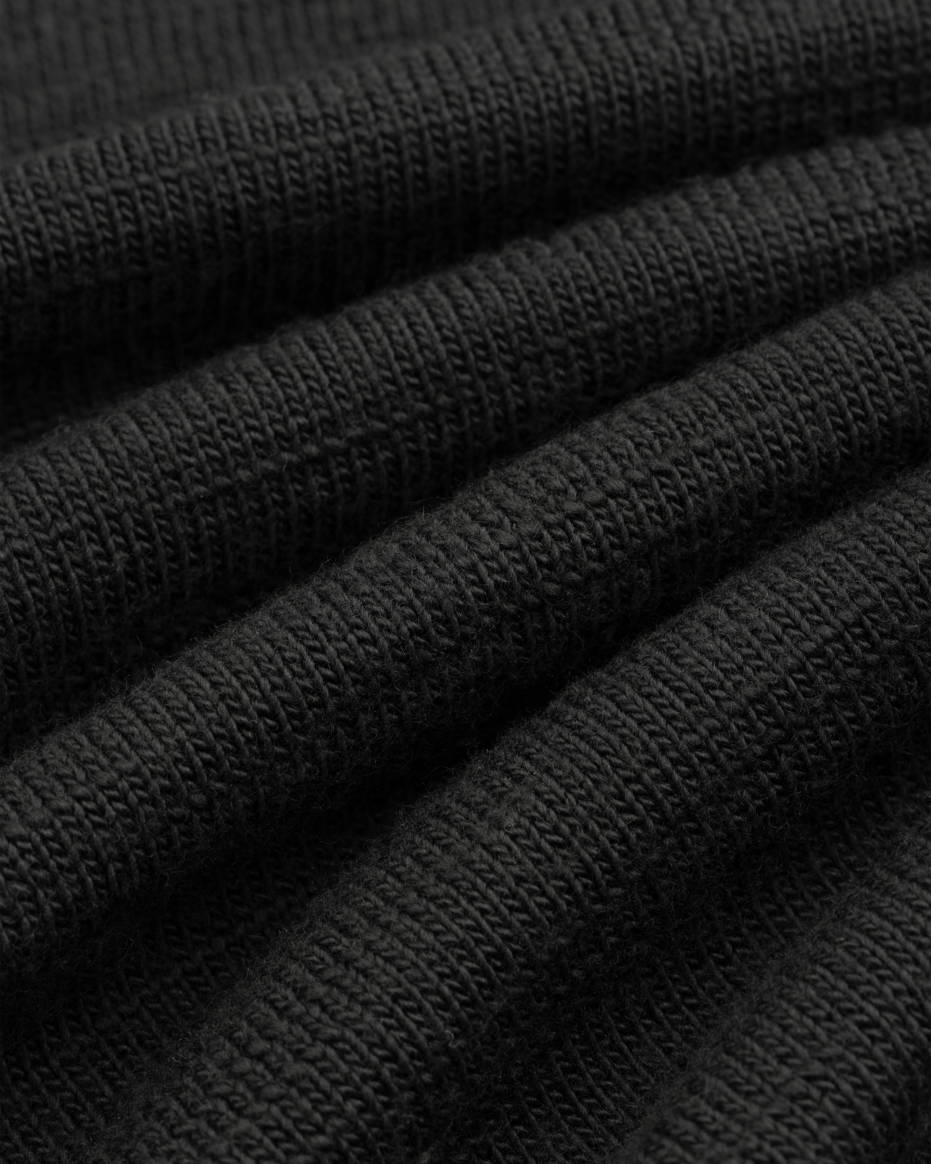 Close-up of the black Slub Merino Wool Sweater, showing its visible knit texture.