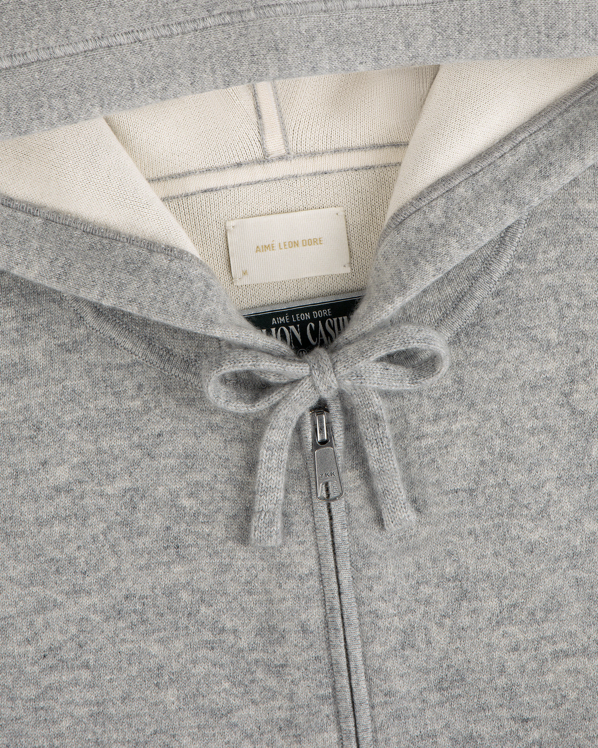 Gray Full-Zip Pavilion Cashmere Hoodie with tied drawstring, cream lining, and Aimé Leon Dore brand label.