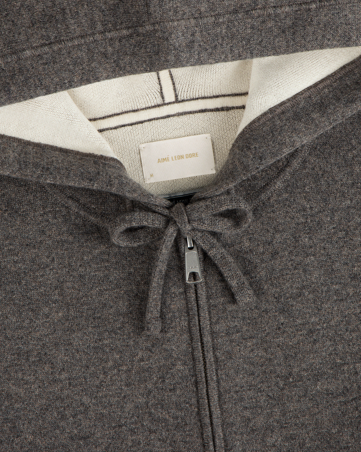 Close-up of the Full-Zip Pavilion Cashmere Hoodie in brown with cream lining, drawstring, and Aimé Leon Dore label.