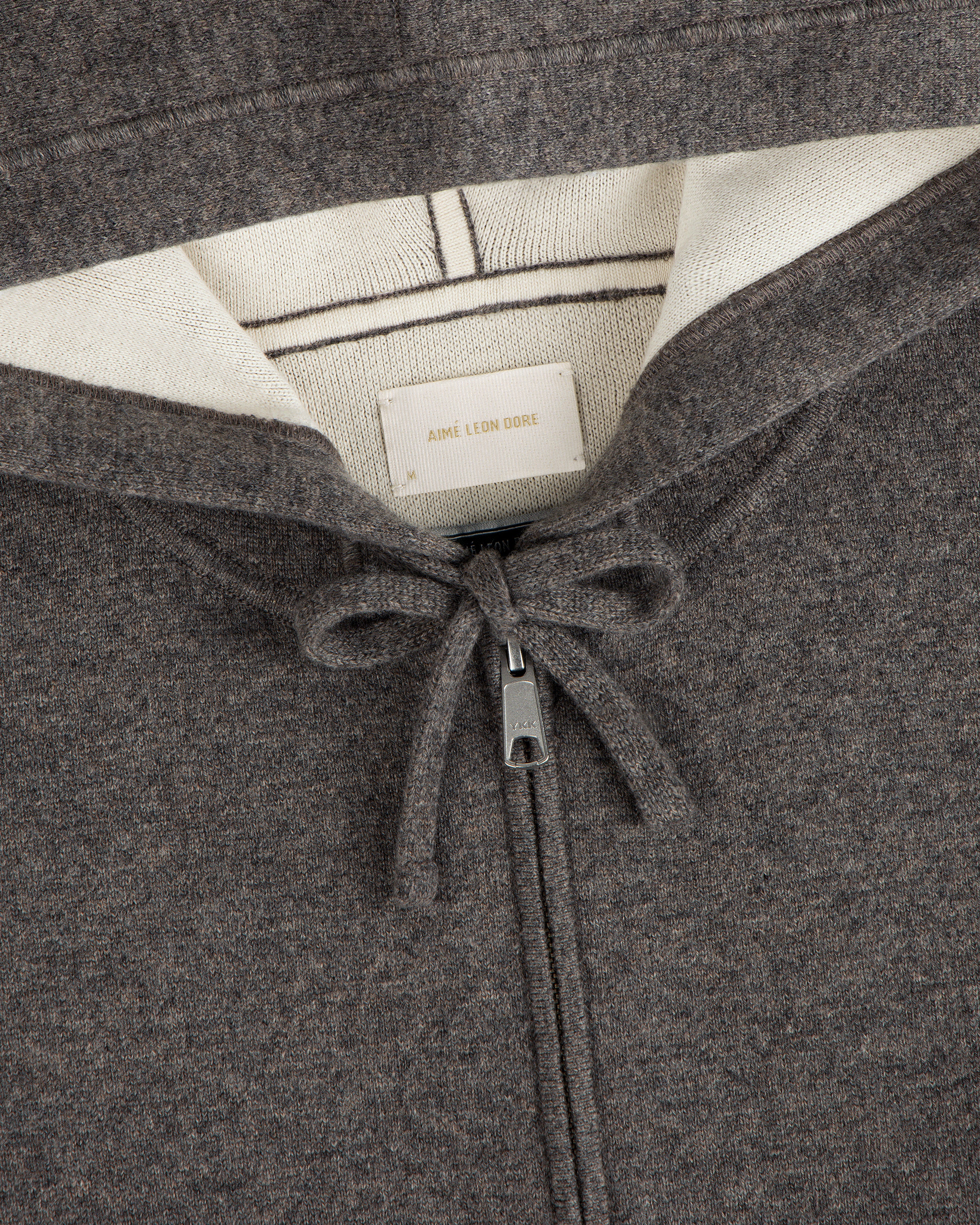 Close-up of the Full-Zip Pavilion Cashmere Hoodie in brown with cream lining, drawstring, and Aimé Leon Dore label.