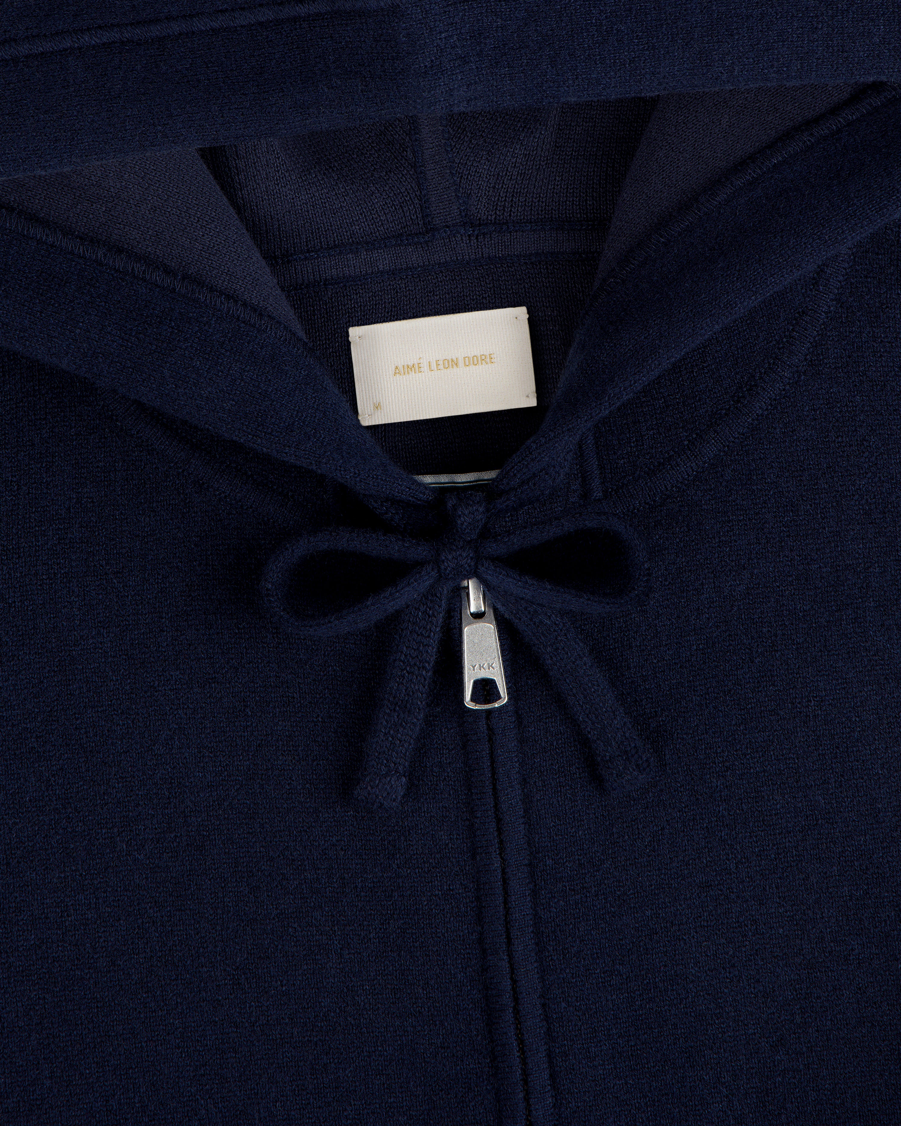 Close-up of the Full-Zip Pavilion Cashmere Hoodie in navy with zipper, drawstring, and Aimé Leon Dore collar label.