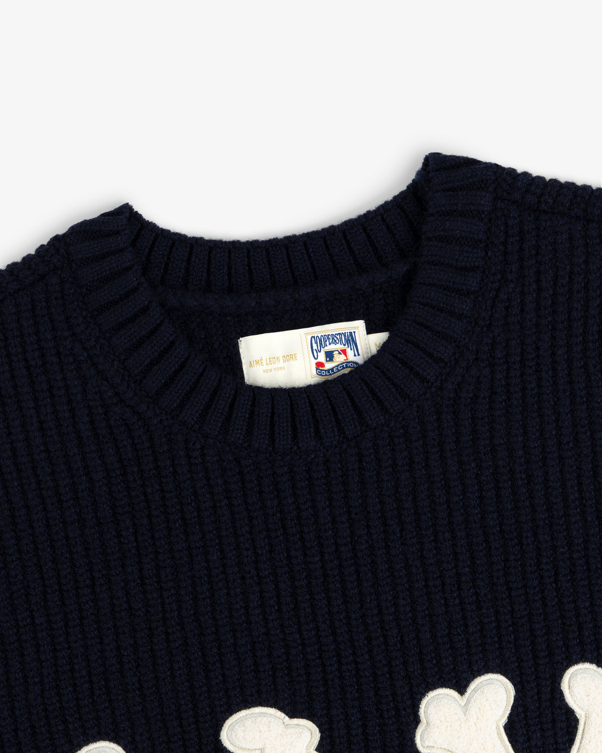 Close-up of NY Highlanders navy ribbed wool crewneck sweater with white label and partial white appliqué design.