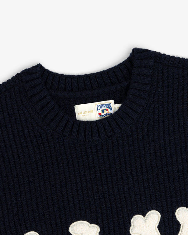 Close-up of NY Highlanders navy ribbed wool crewneck sweater with white label and partial white appliqué design.