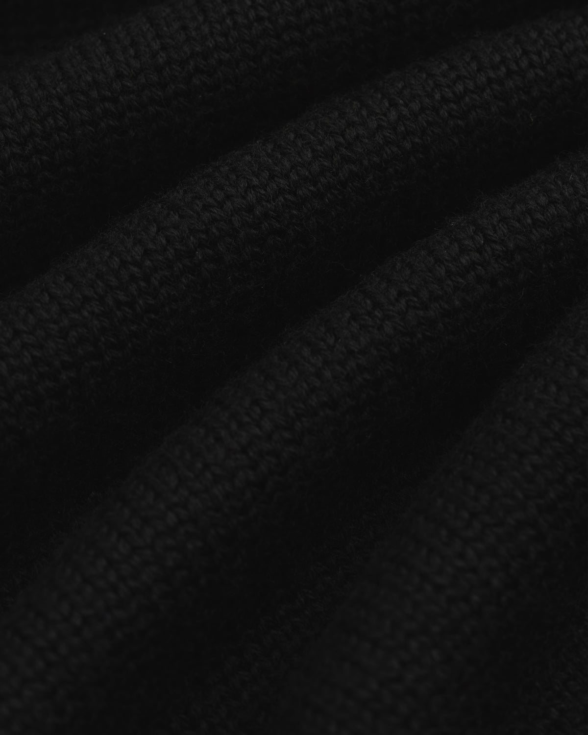 Close-up of black knit fabric from a Long-Sleeve Merino Polo with visible horizontal folds.