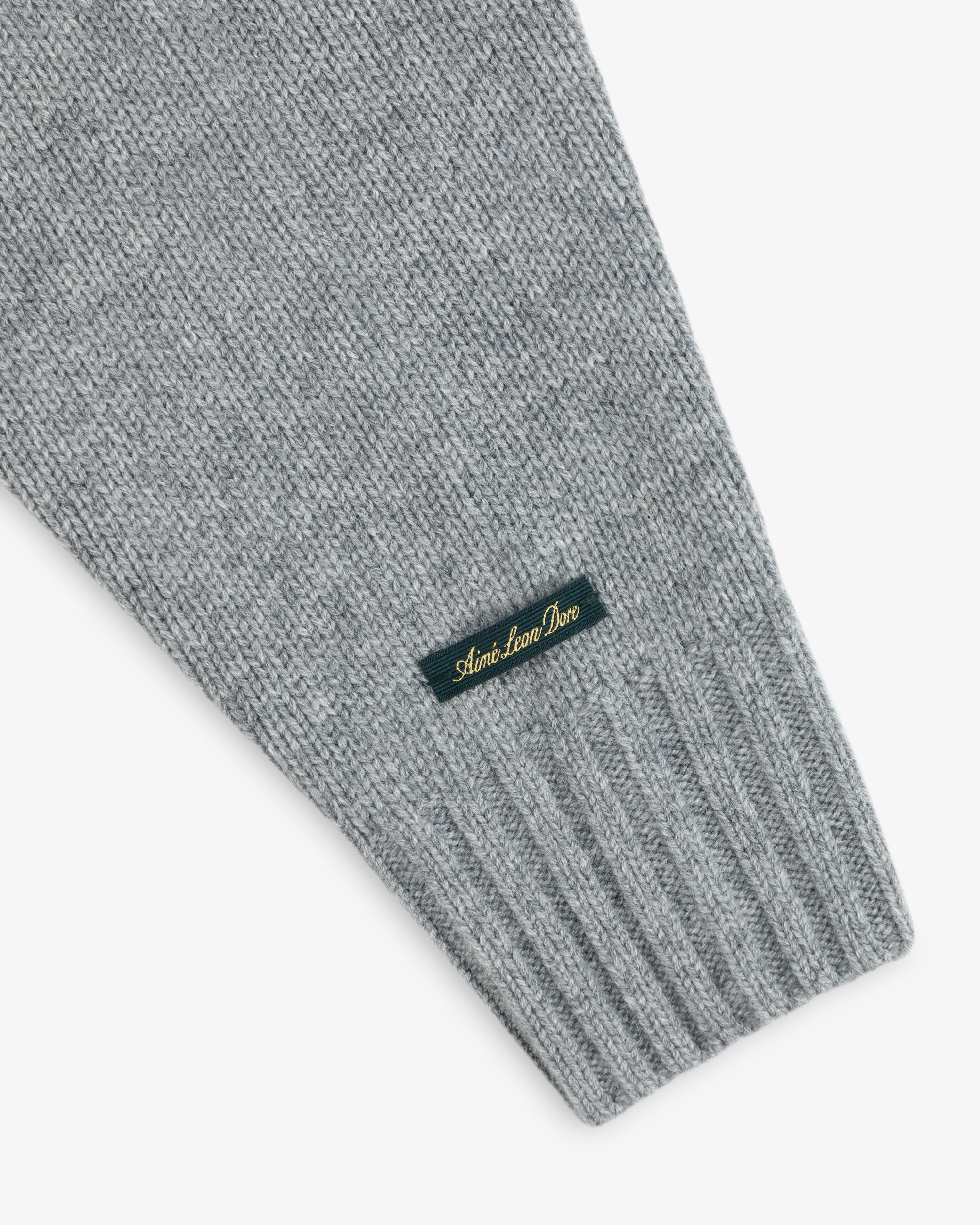 Grey Cashmere Crewneck Sweater sleeve with a ribbed cuff and a small woven tag featuring gold cursive text.