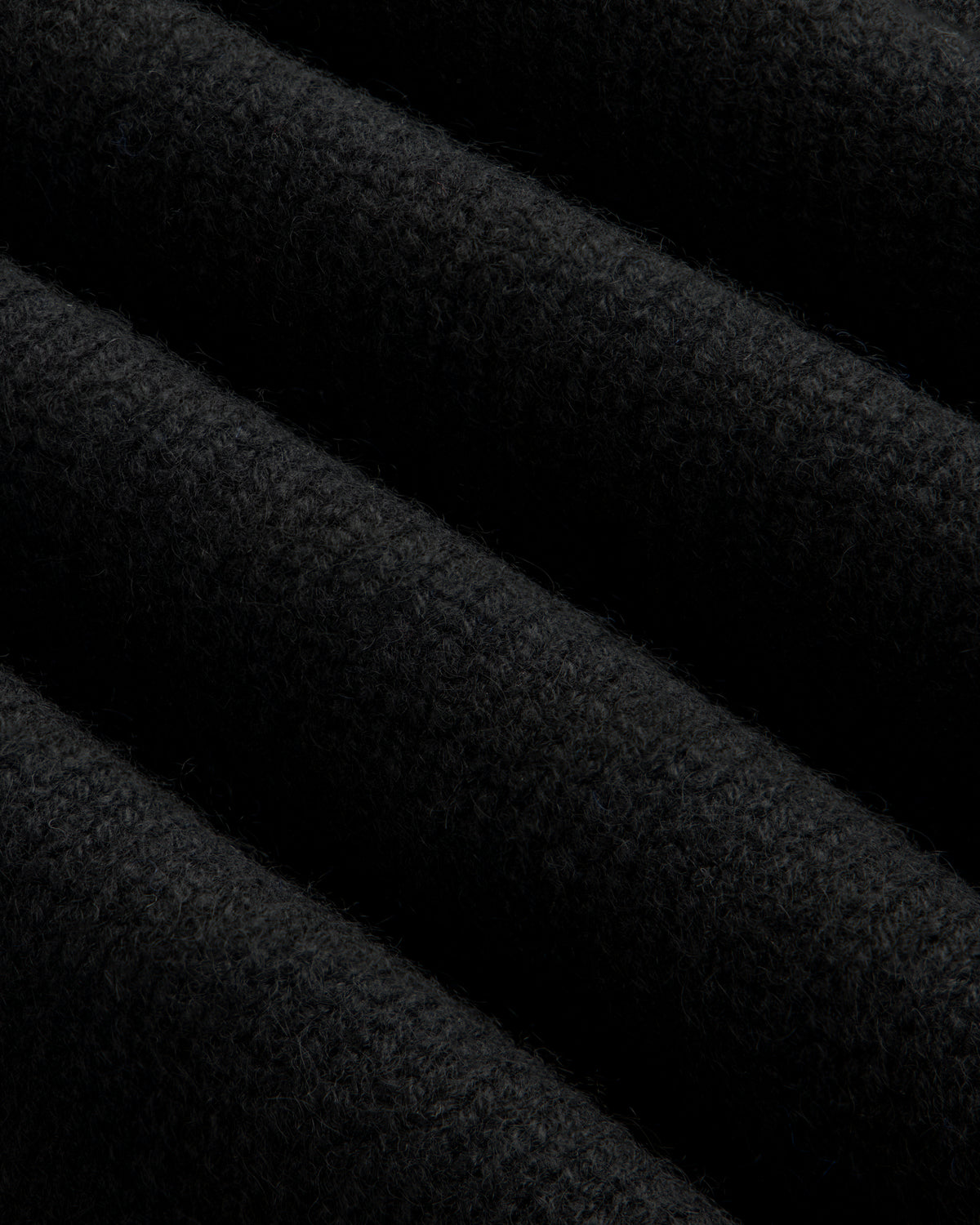 Close-up of a black Cashmere Crewneck Sweater showing diagonal folds in the knit fabric.