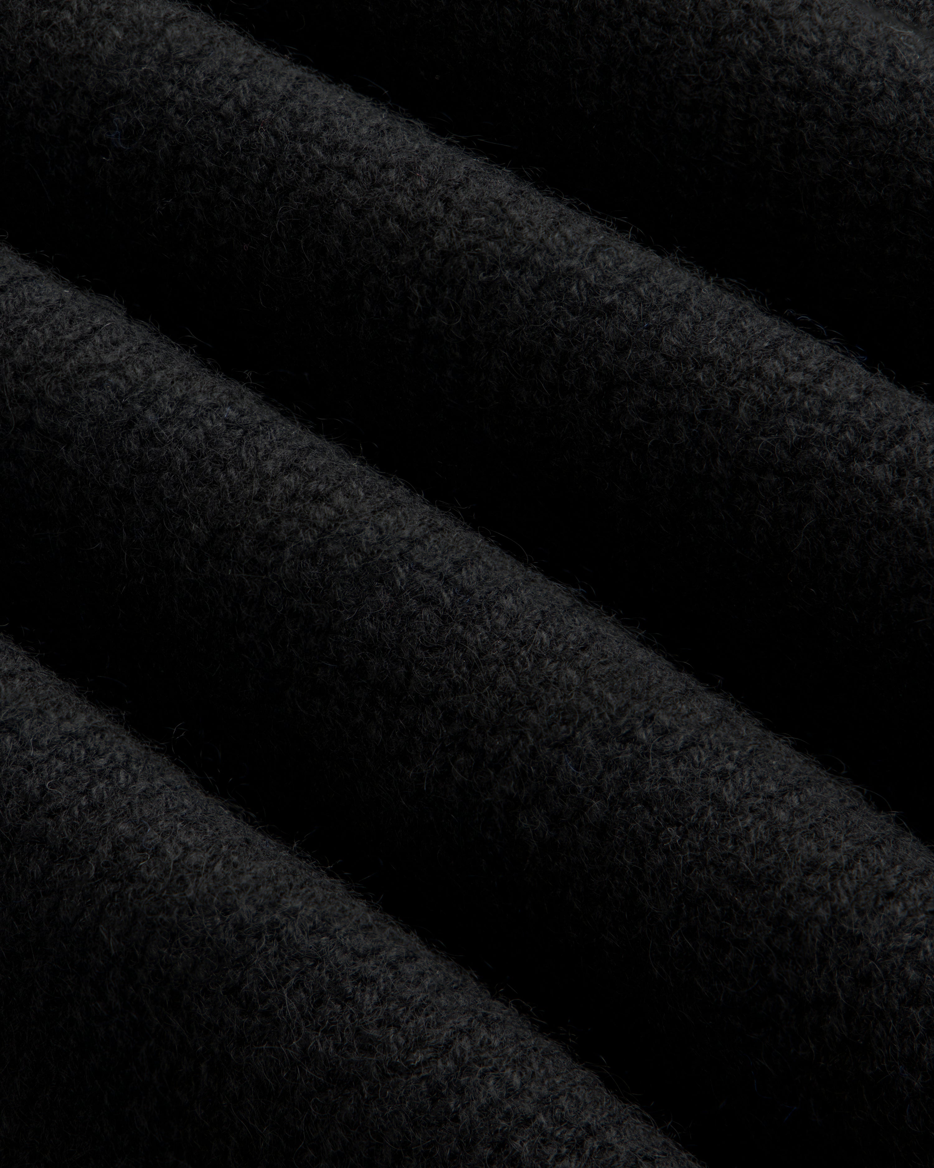 Close-up of a black Cashmere Crewneck Sweater showing diagonal folds in the knit fabric.