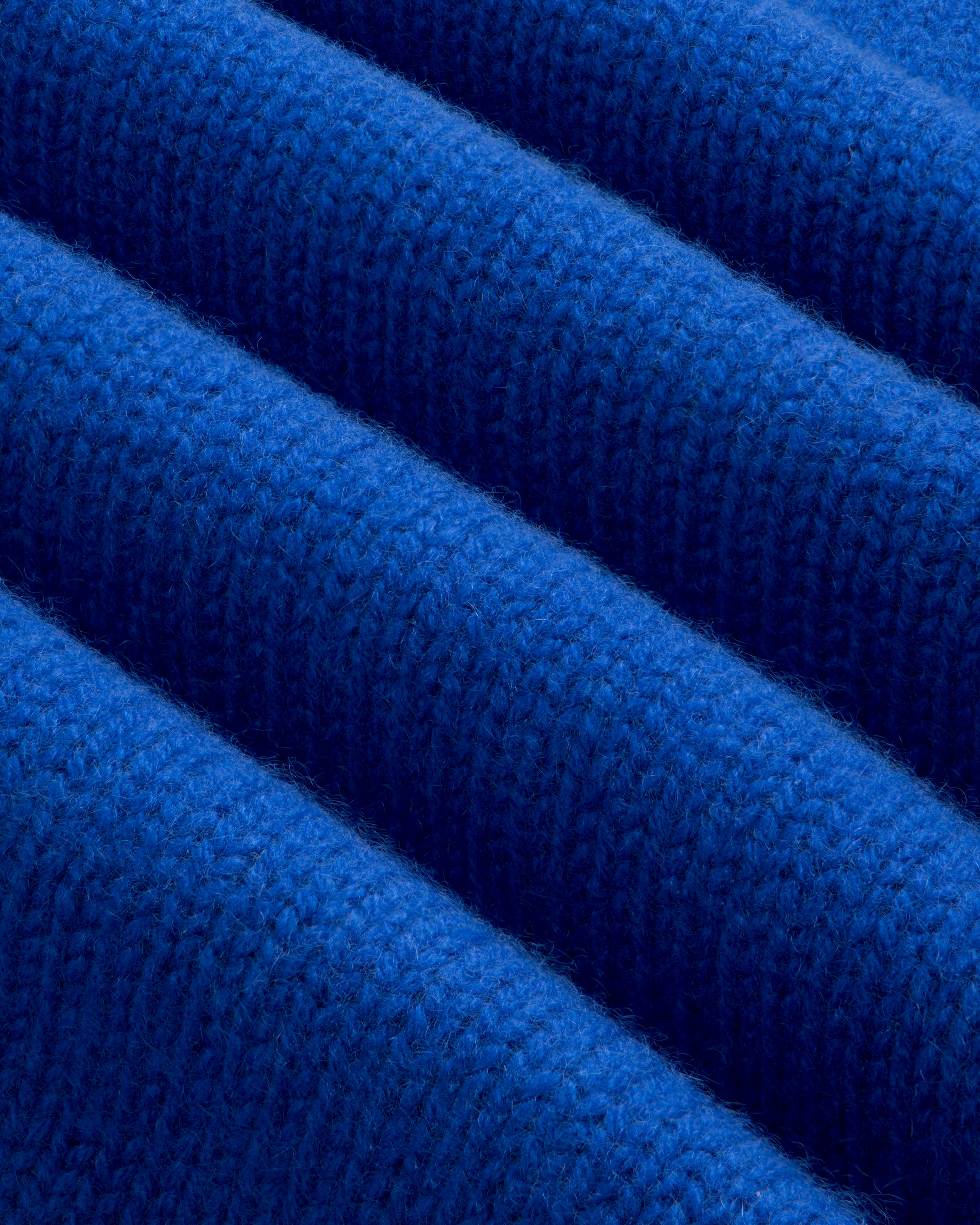Close-up of bright blue Cashmere Crewneck Sweater knit fabric folded in parallel ridges.