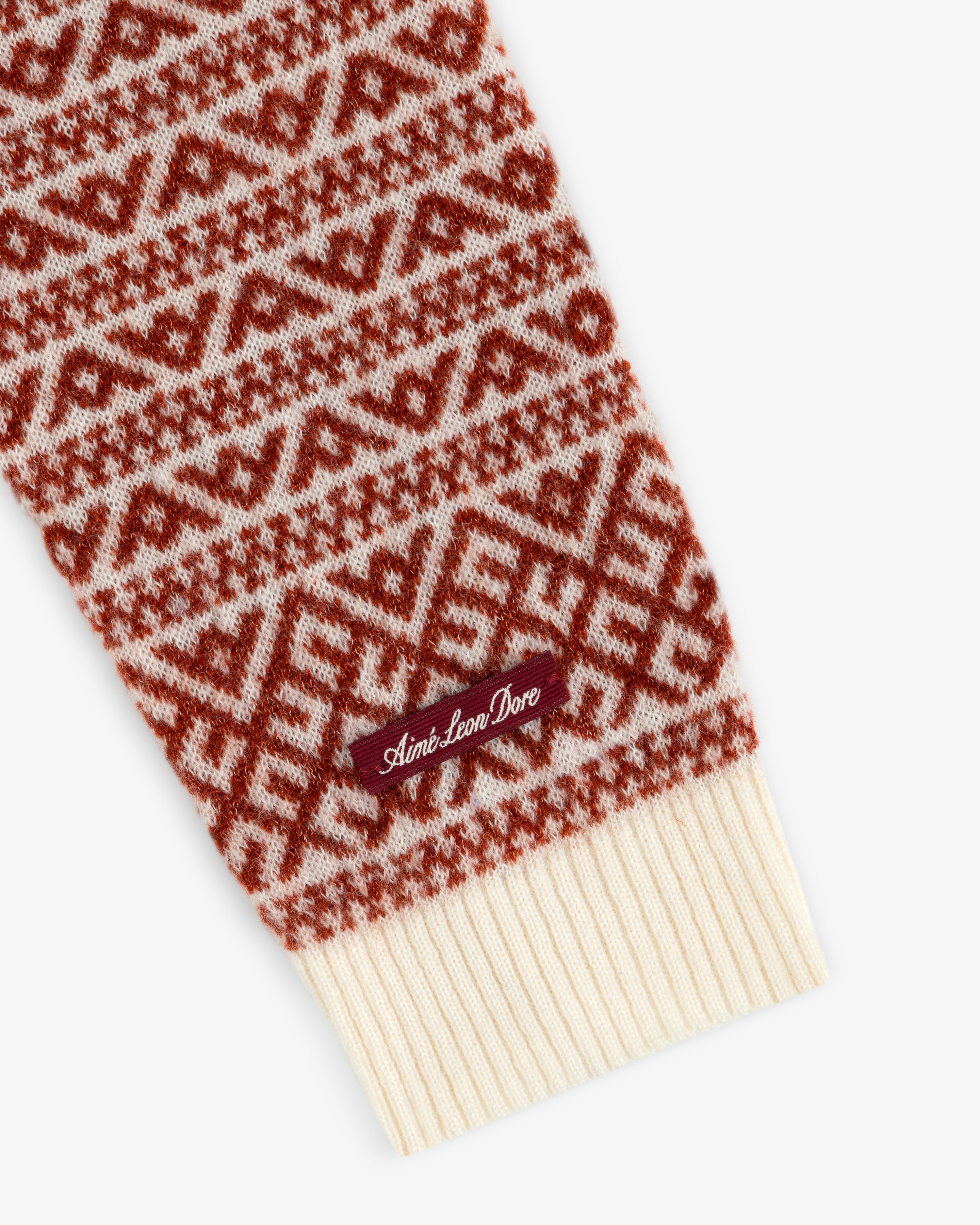 Close-up of a Wool Cashmere Jacquard Cardigan sleeve in a rust and cream geometric pattern with a brand tag on the cuff.
