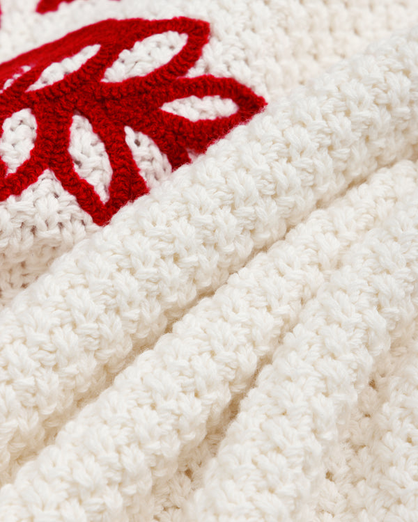 Close-up of a white ALD / Olympiacos F.C. Knit V-Neck Sweater with a red embroidered floral or emblem design.