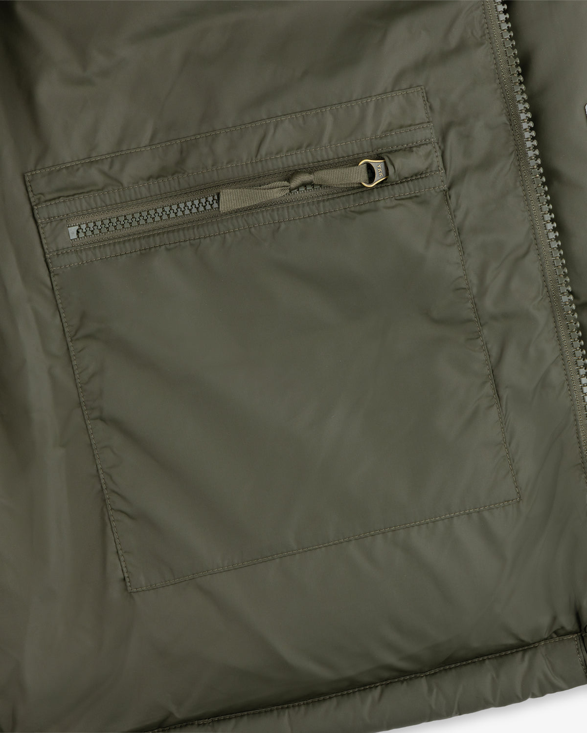 Close-up of an ALD / The North Face Baltoro Jacket pocket in olive green, featuring a horizontal zipper and stitching.