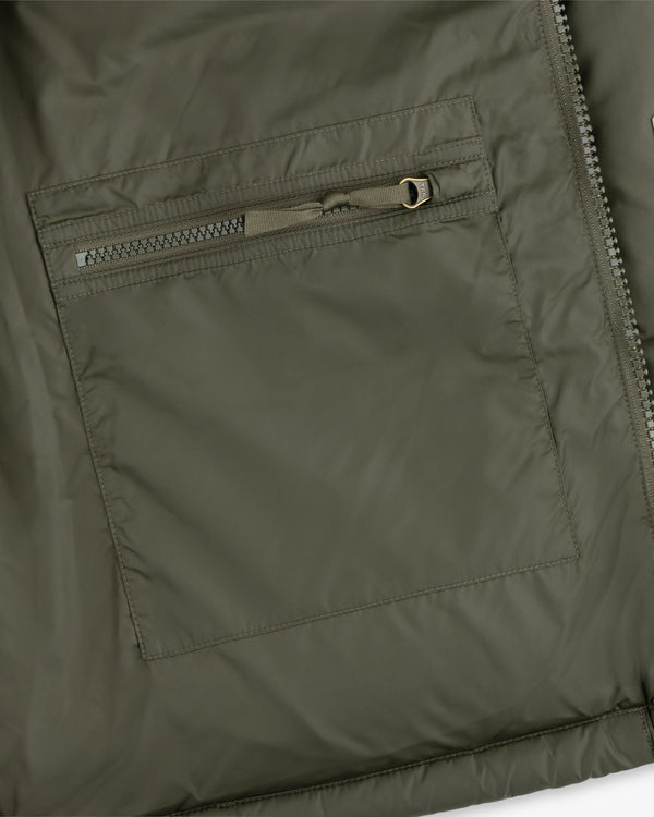 Close-up of an ALD / The North Face Baltoro Jacket pocket in olive green, featuring a horizontal zipper and stitching.